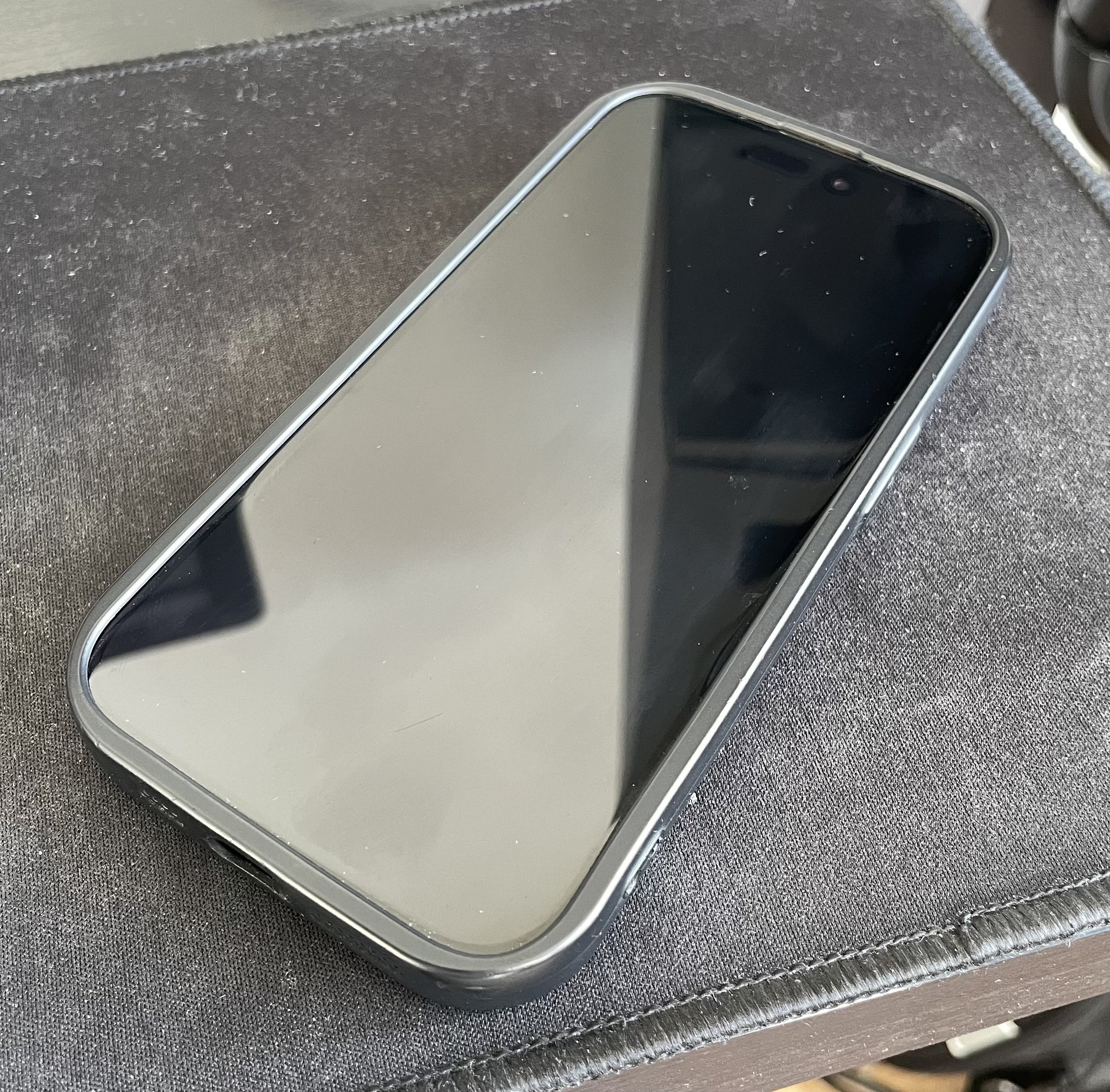 A modern smartphone with a large black screen lying face up on a dark fabric surface.