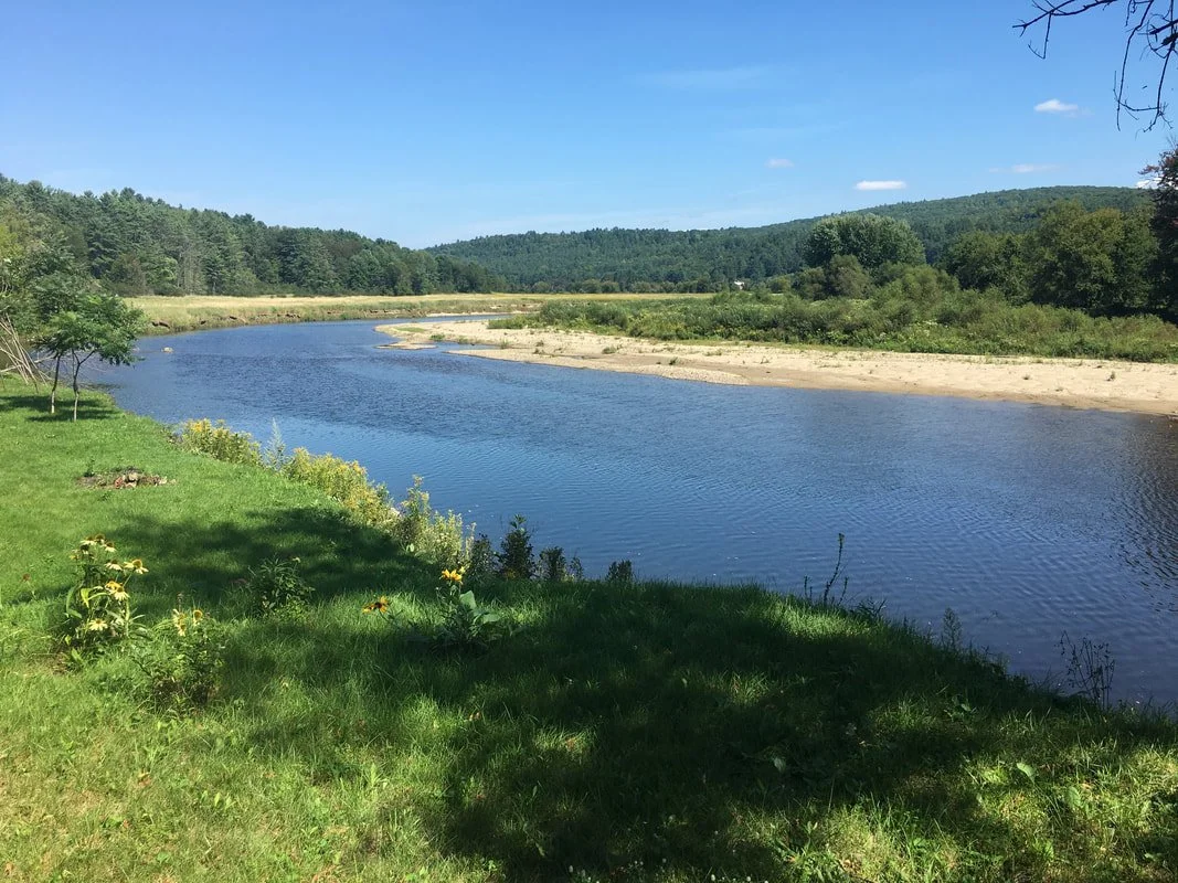 A calm river curves through a green landscape with trees and hills in the background on a sunny day.