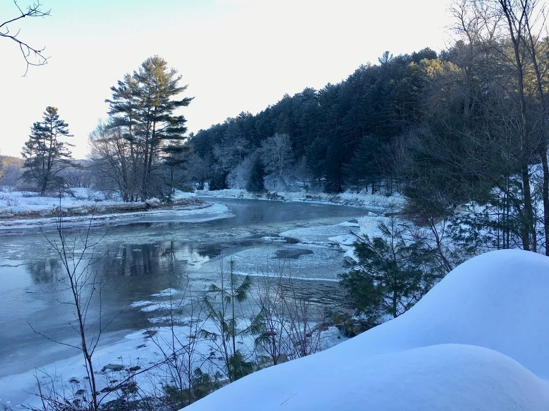 Snow-covered landscape with a partially frozen river surrounded by trees in winter.