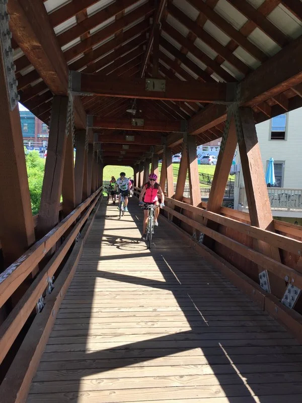 People riding bicycles on a wooden covered bridge on a sunny day.