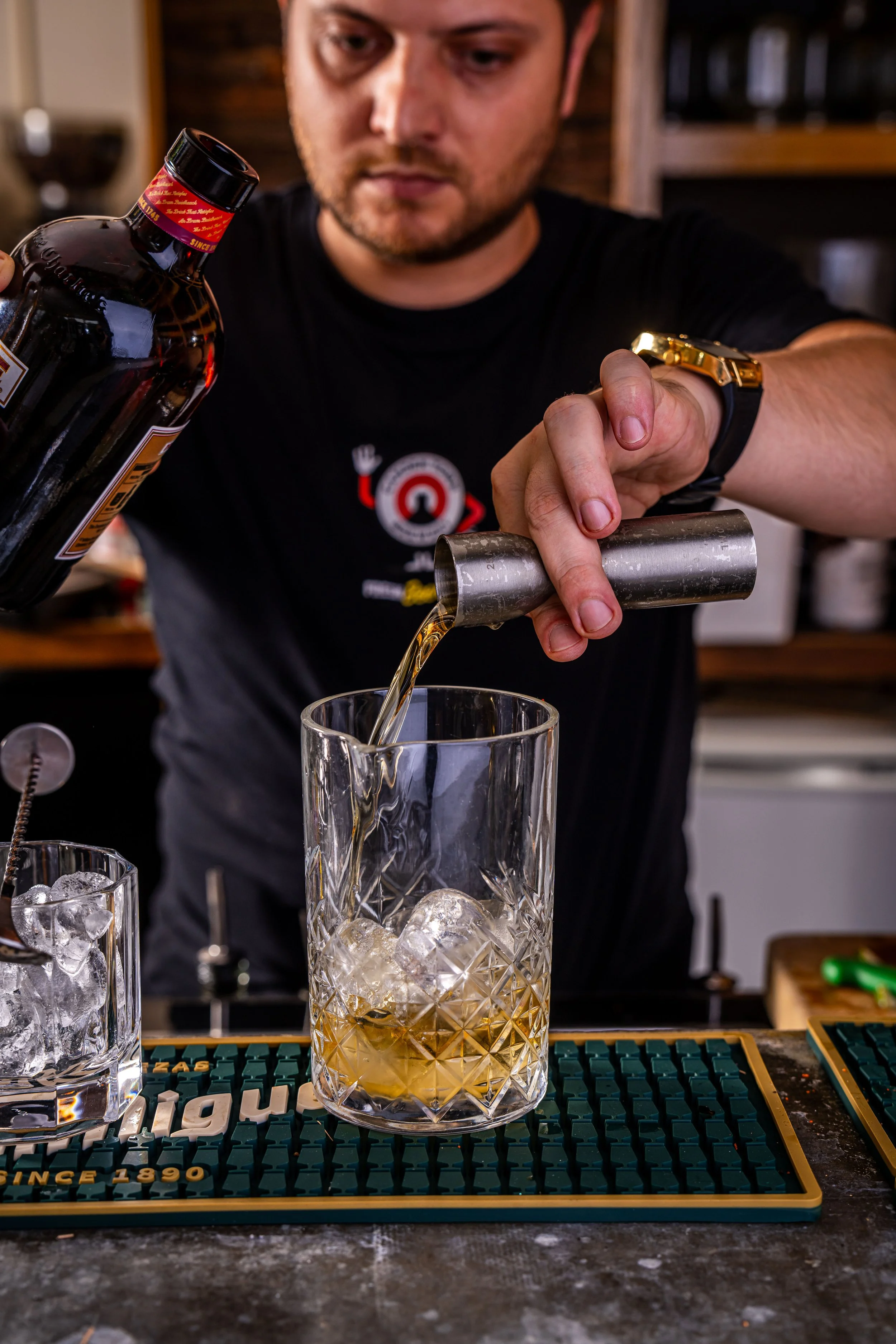A bartender pours whiskey over ice into a glass with a textured pattern.