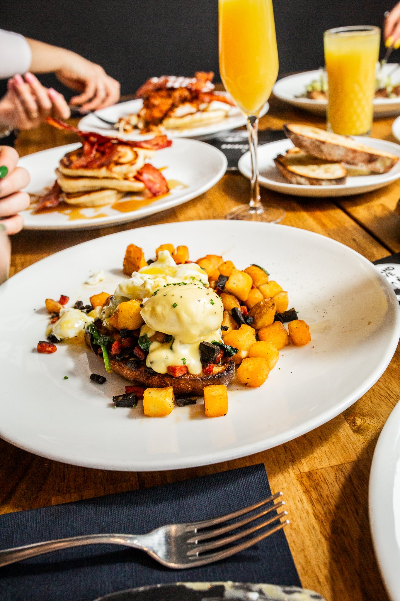 Plate of eggs Benedict with roasted potatoes and chopped herbs on a white plate.