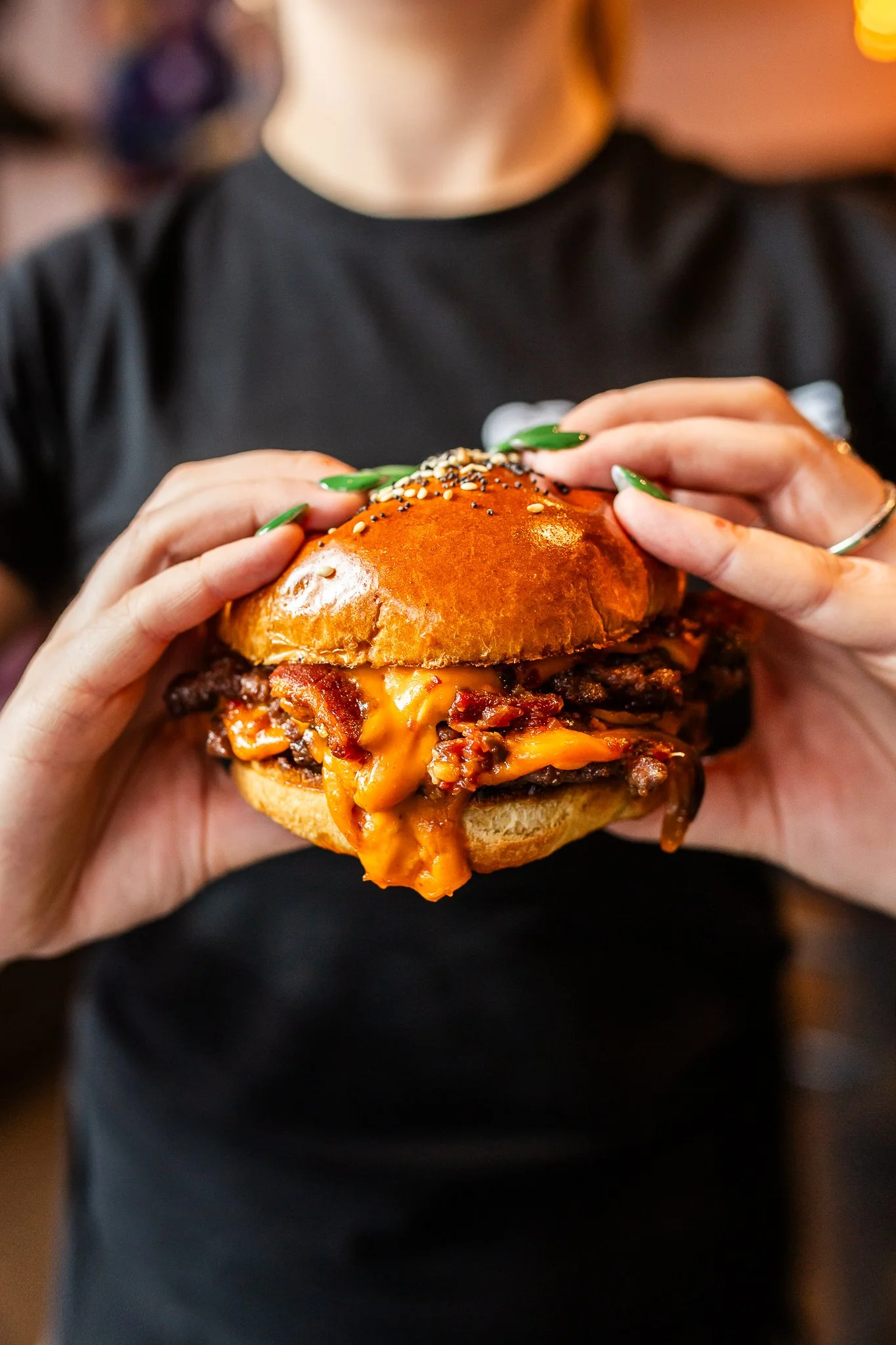 Person holding a cheeseburger with bacon, melted cheese, and a shiny bun.