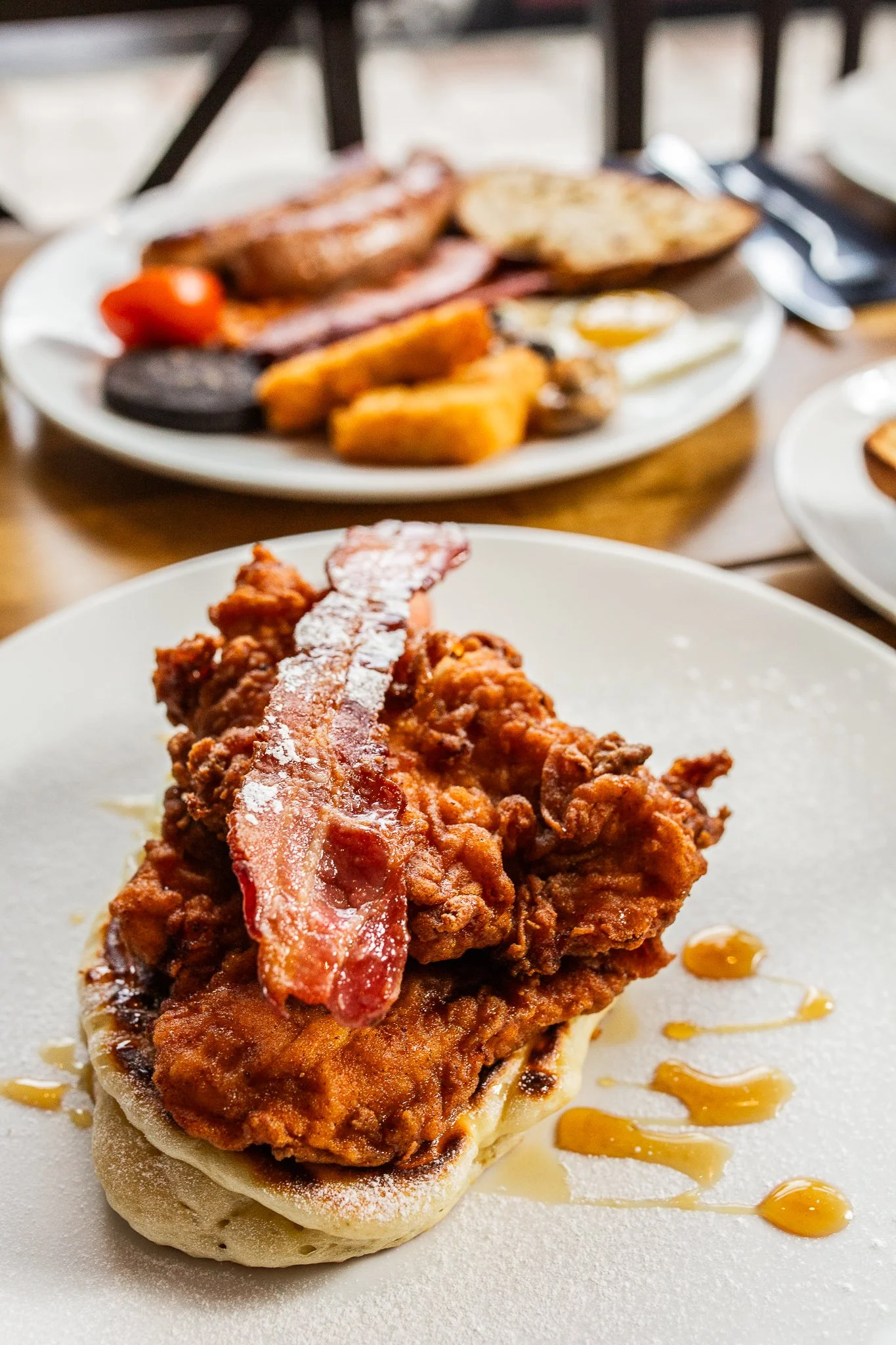 Close-up of fried chicken and bacon served on a biscuit with syrup drizzled on the plate.