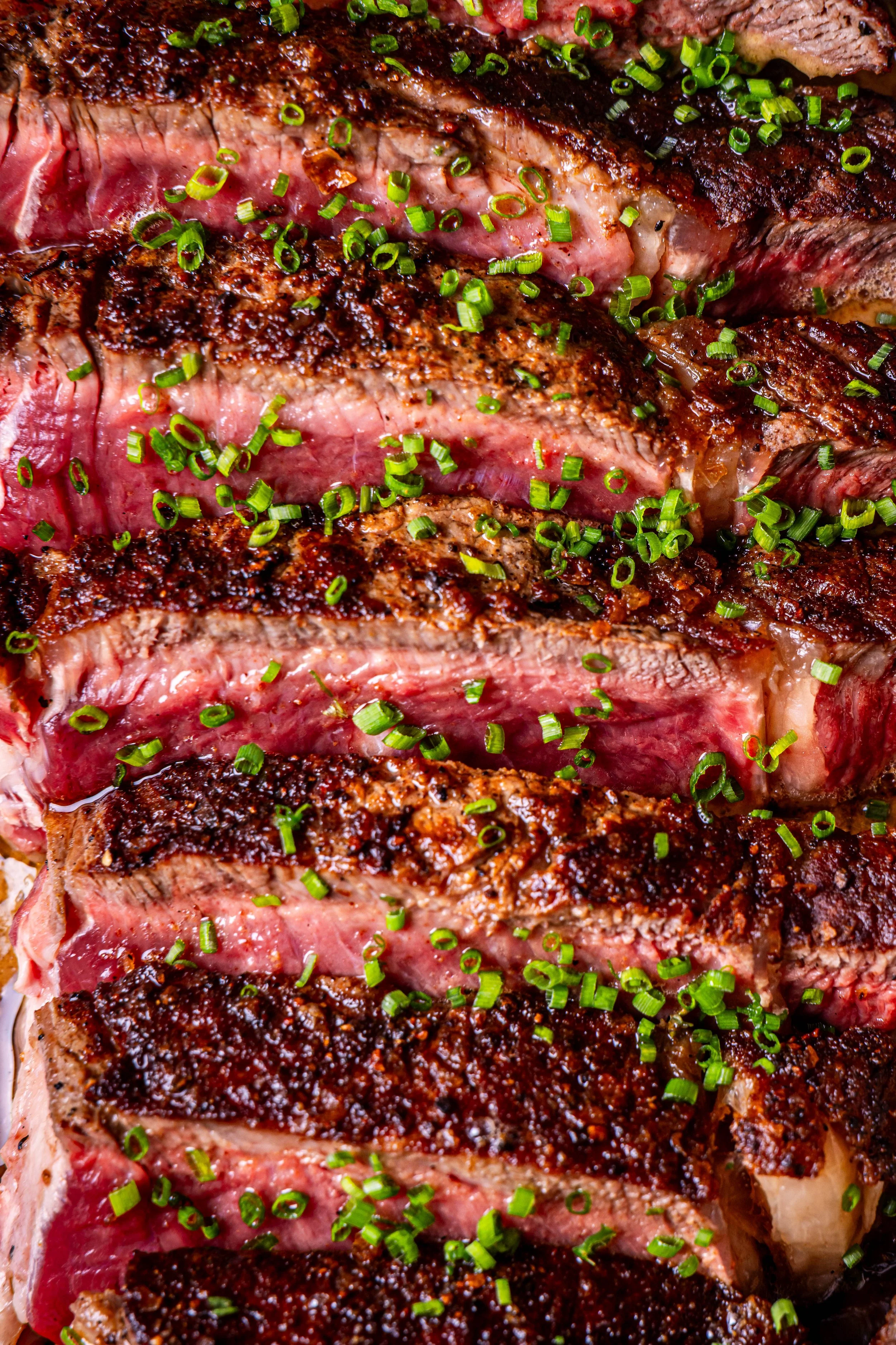 Close-up of sliced medium-rare steak garnished with chopped green onions.