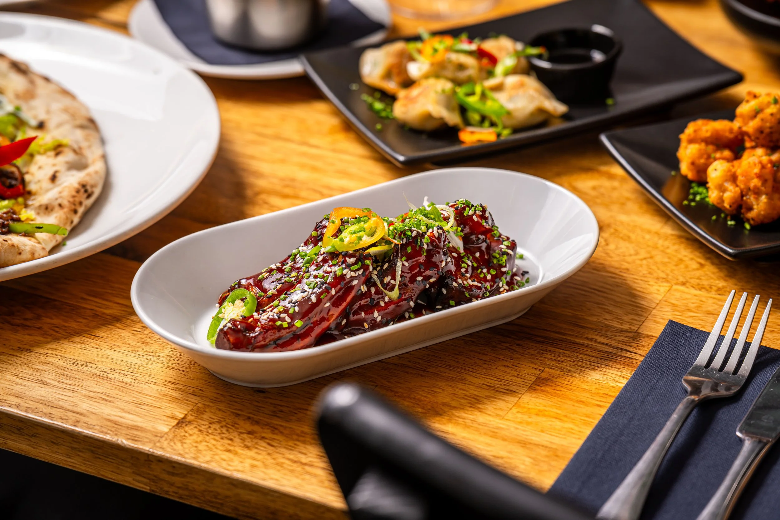 Dish of glazed beef ribs garnished with chopped green onions on a white oval plate
