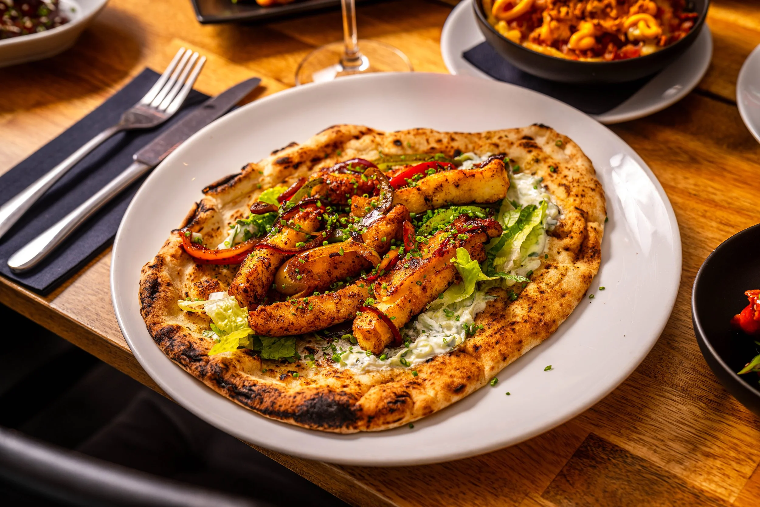 Gyros with grilled chicken, red peppers, lettuce, and herbs, served on a wooden table.