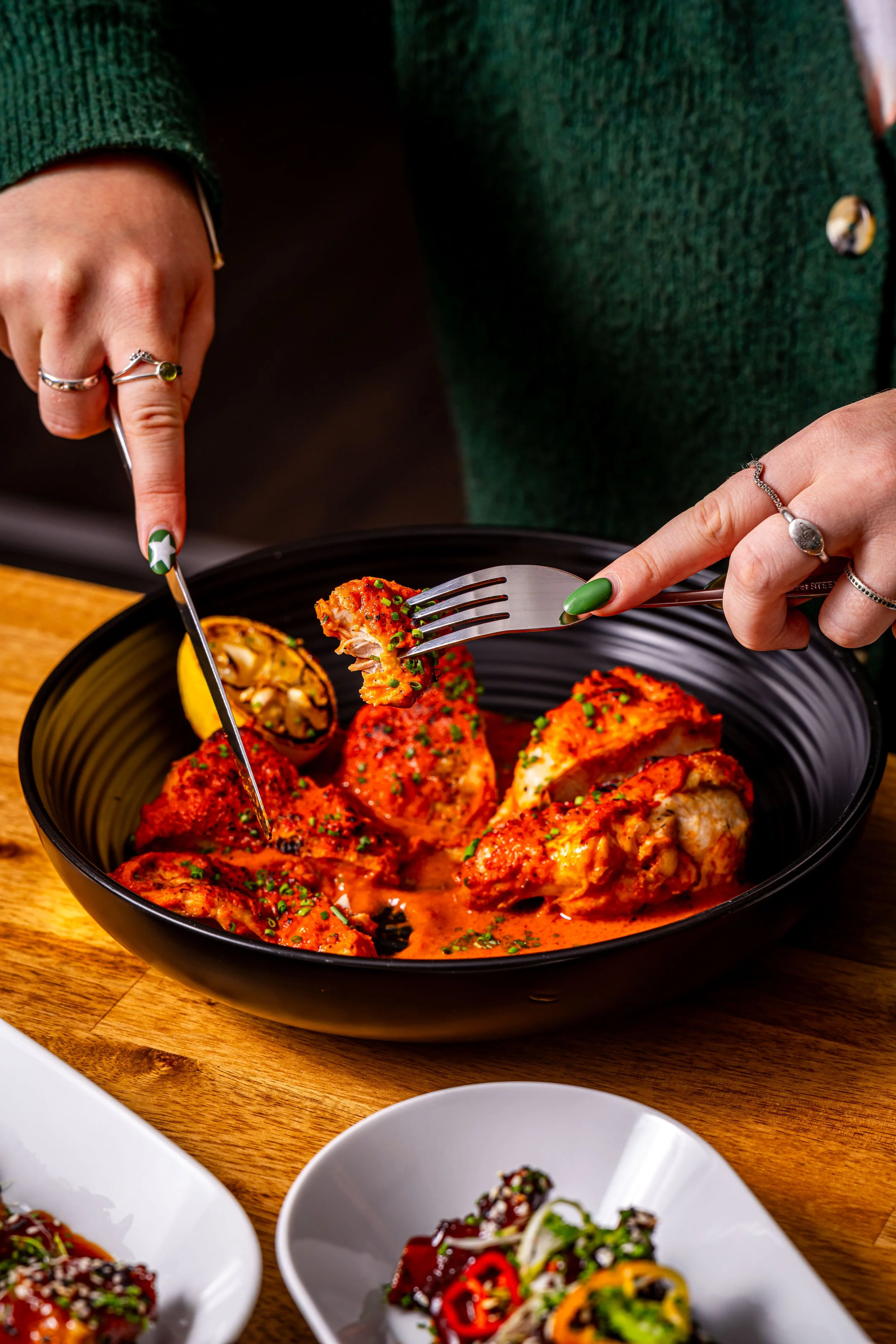 Person serving spicy glazed chicken wings with a fork and knife at a wooden table.