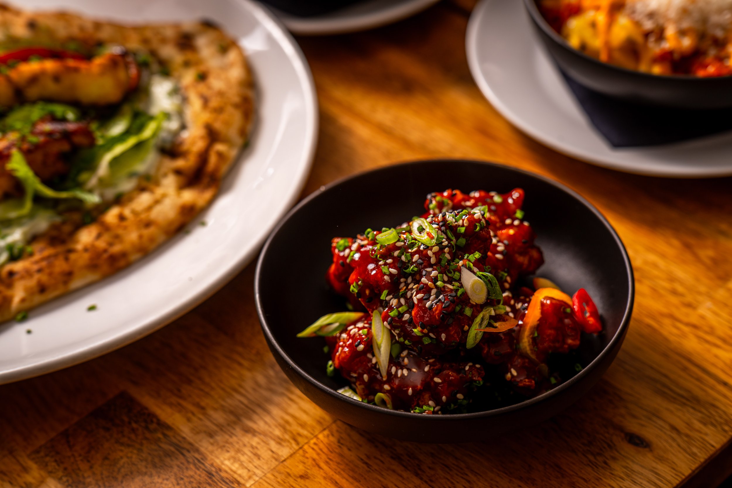 Spicy Korean chicken wings garnished with chopped green onions and sesame seeds, served in a black bowl on a wooden table.