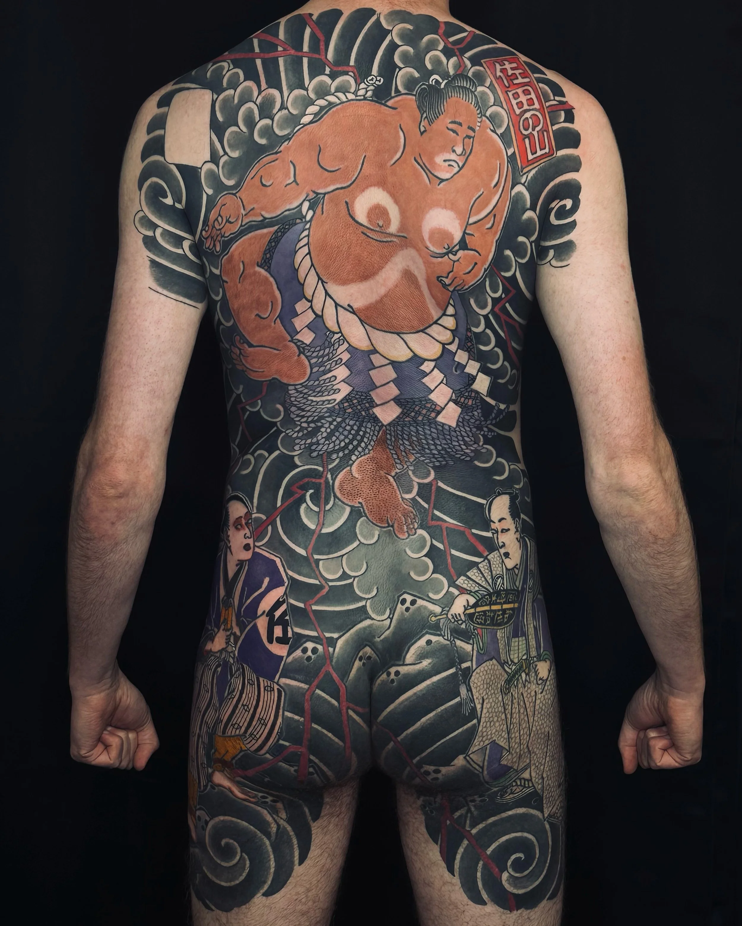 Tatouage traditionnel japonais couvrant le dos et les bras, représentant une figure masculine en style ukiyo-e avec des éléments de nuages noirs et colorés.