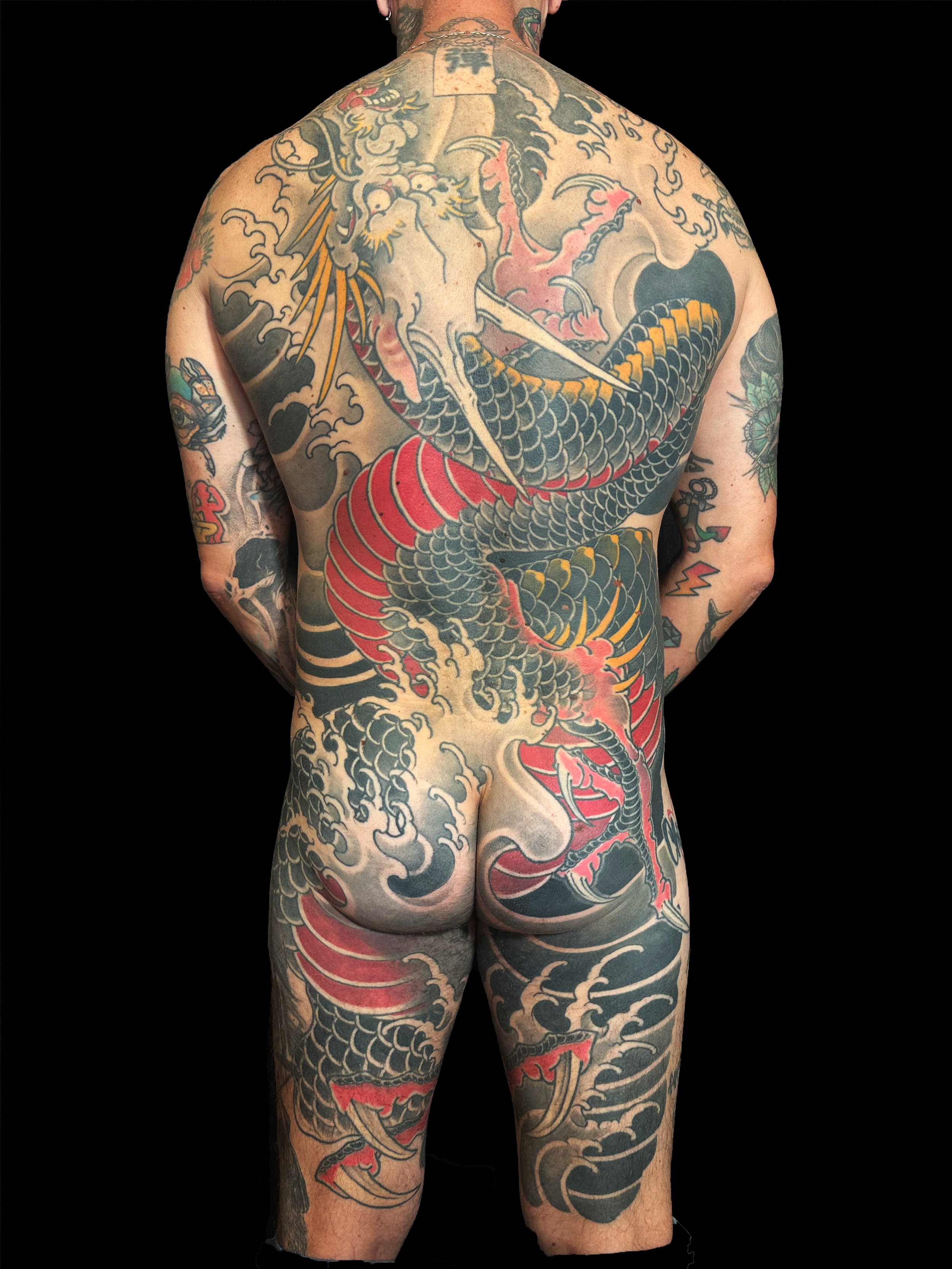 Un homme avec de nombreuses tatouages traditionnels japonais couvrant toute son dos, ses bras et ses jambes, représentant un dragon et d'autres motifs.