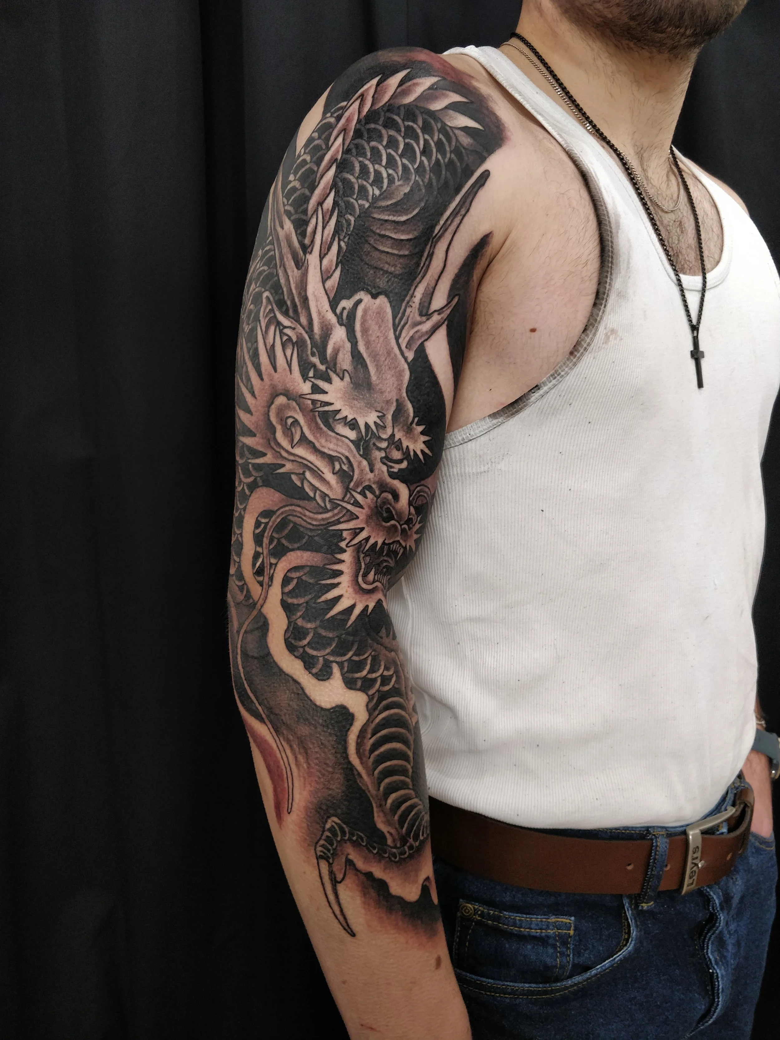 Un homme portant un gilet blanc avec des tatouages noirs et gris d'un dragon sur le bras gauche.