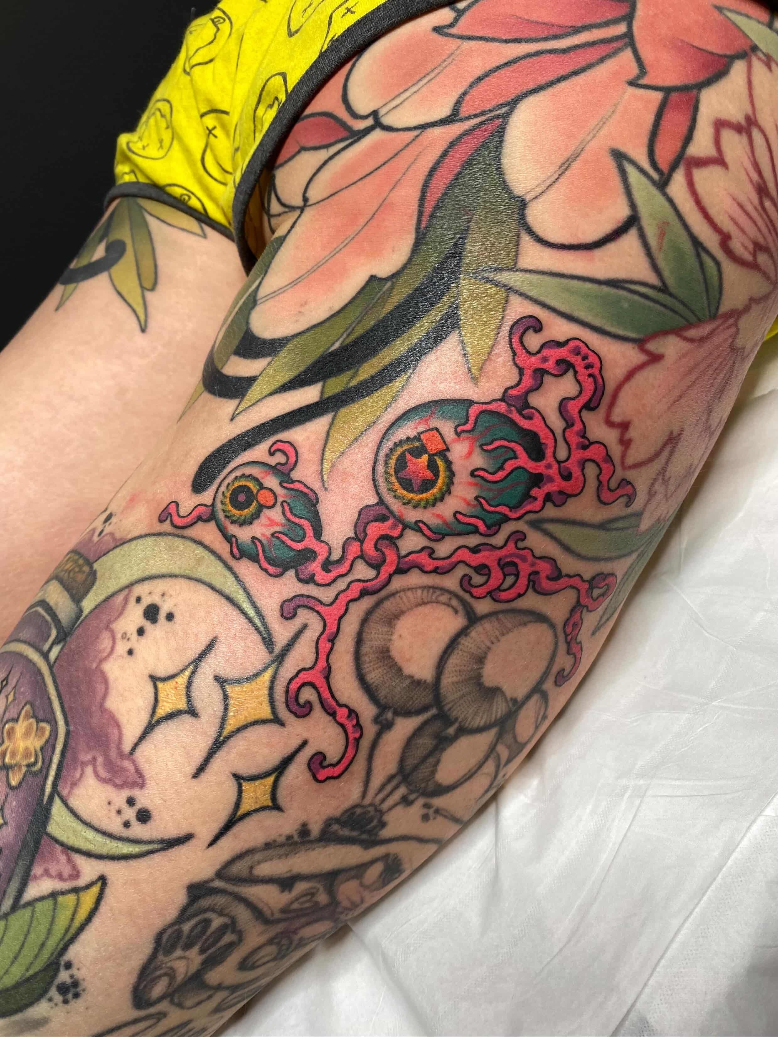 Tatouage coloré de fleurs, yeux et autres motifs distincts sur un bras.