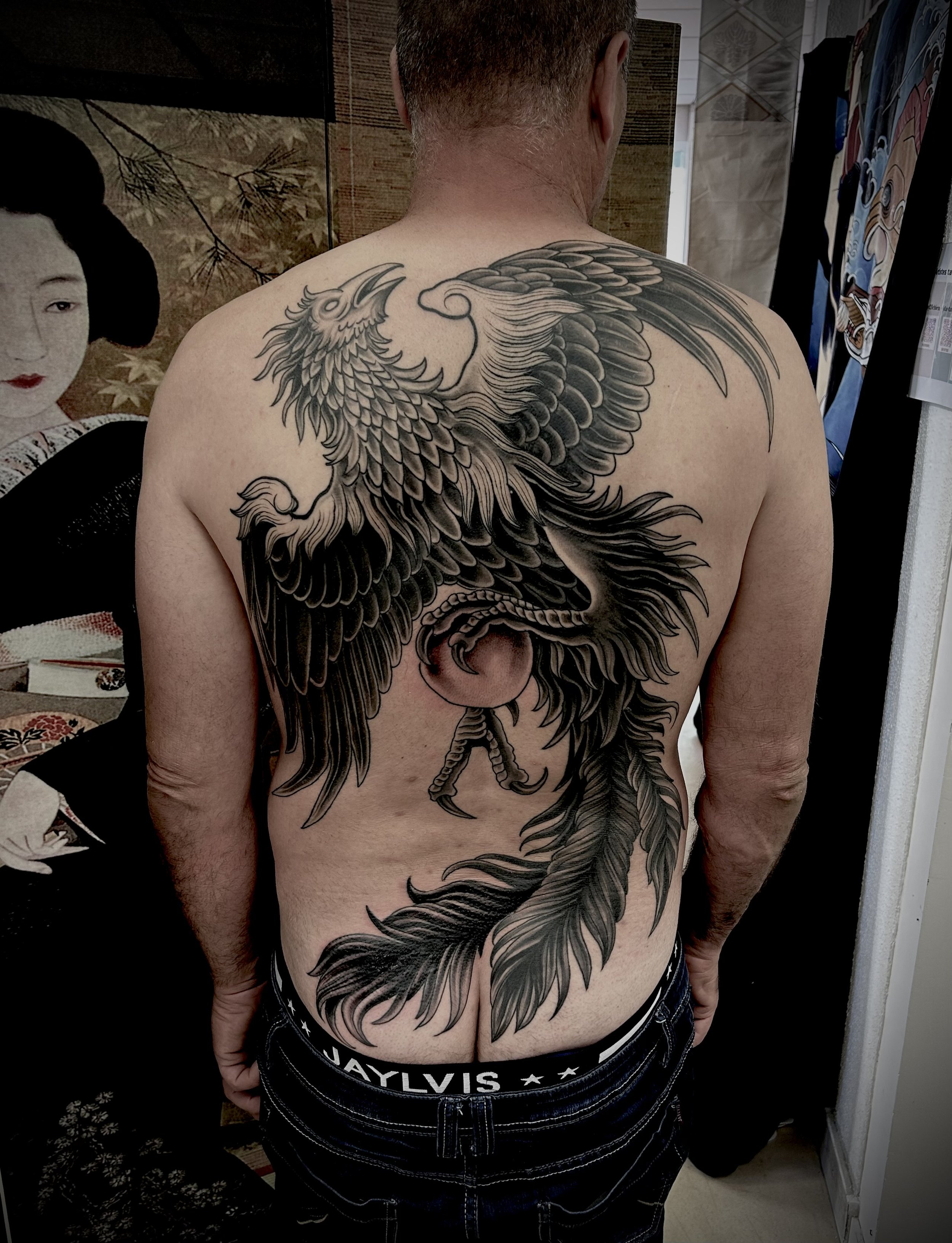 Tatouage de style japonais d'un phénix sur le dos d'un homme, en noir et gris, avec des détails fins et des plumes
