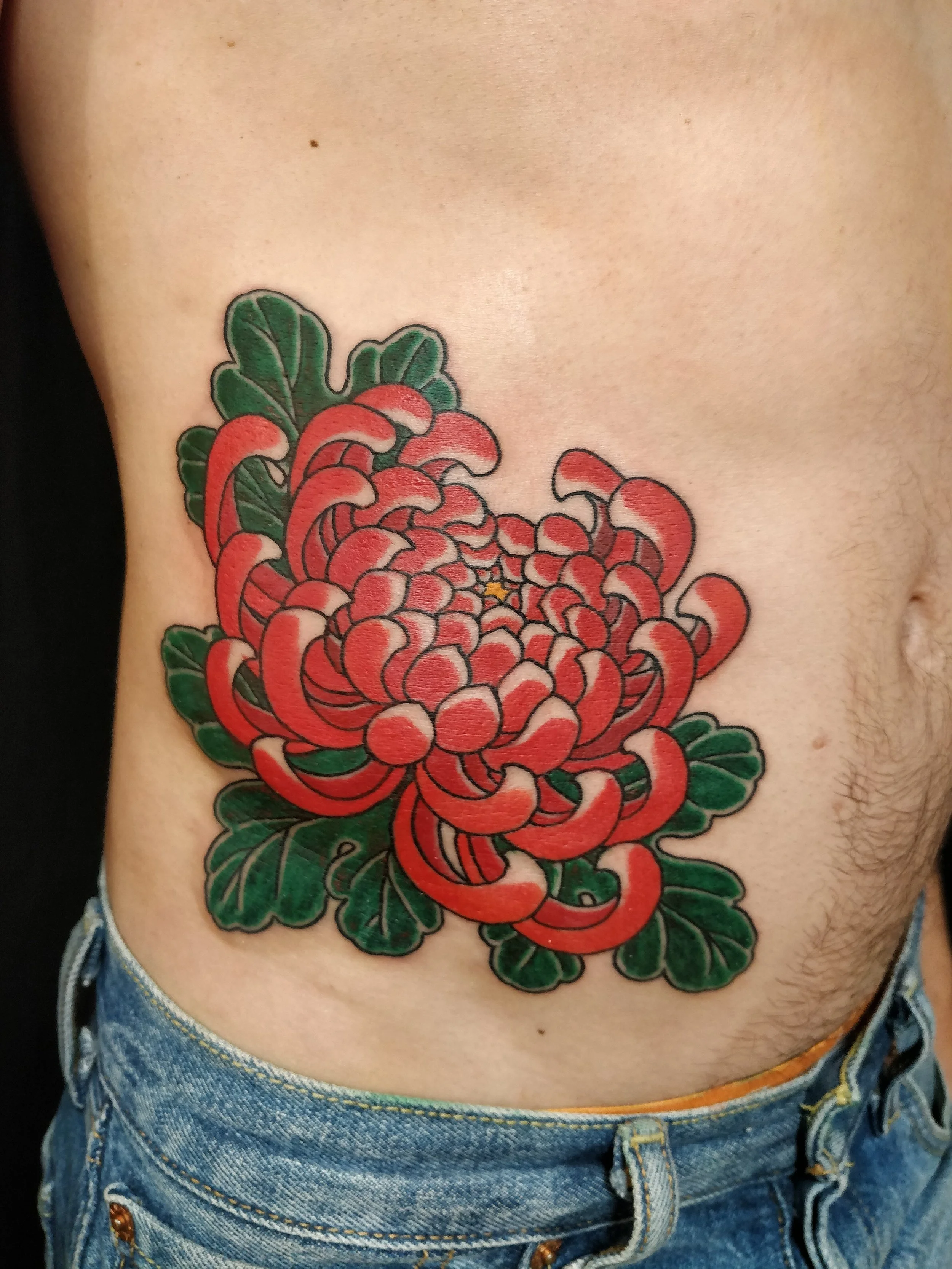 Un tatouage floral coloré sur le côté de la poitrine d'une personne avec un jean bleu.