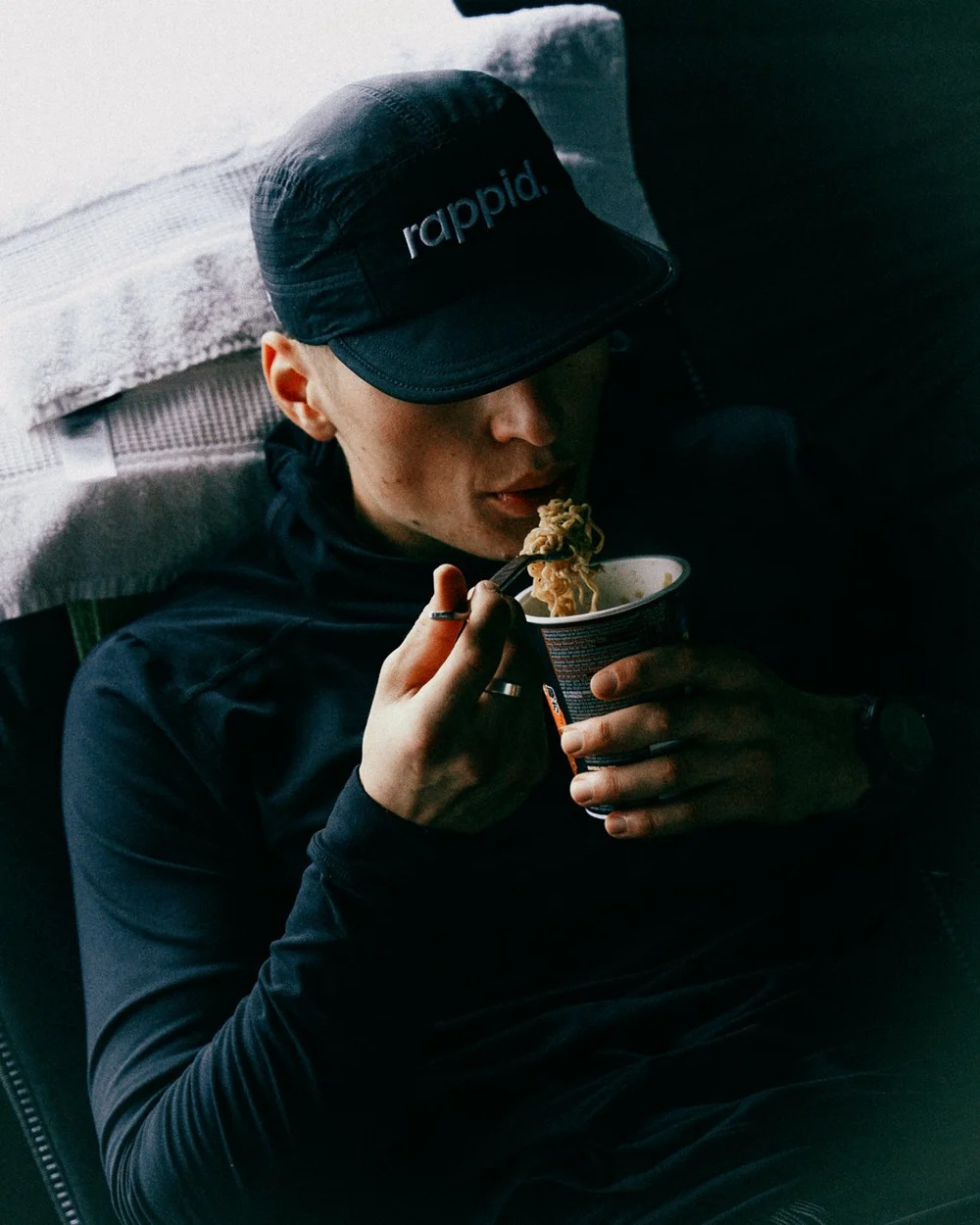 A runner in a rappid. cap eating instant noodles from a cup, resting between laps