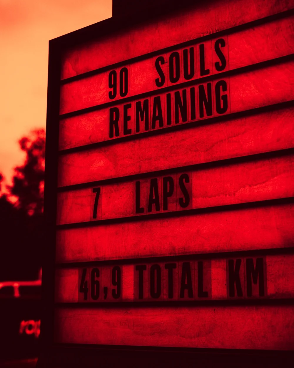The race board lit red at dusk, reading 90 souls remaining, 7 laps, 46.9 total km