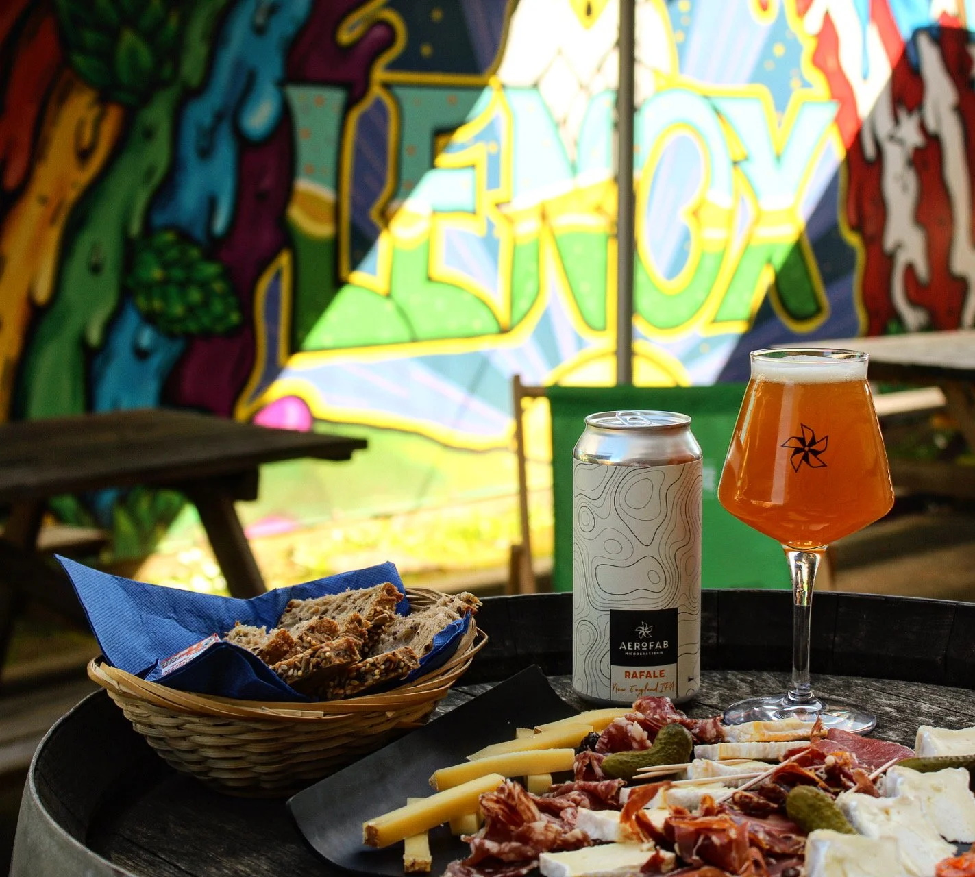 Une pizza sur une table, une canette de boisson, un verre de bière, des morceaux de pain, dans un décor coloré de graffiti.