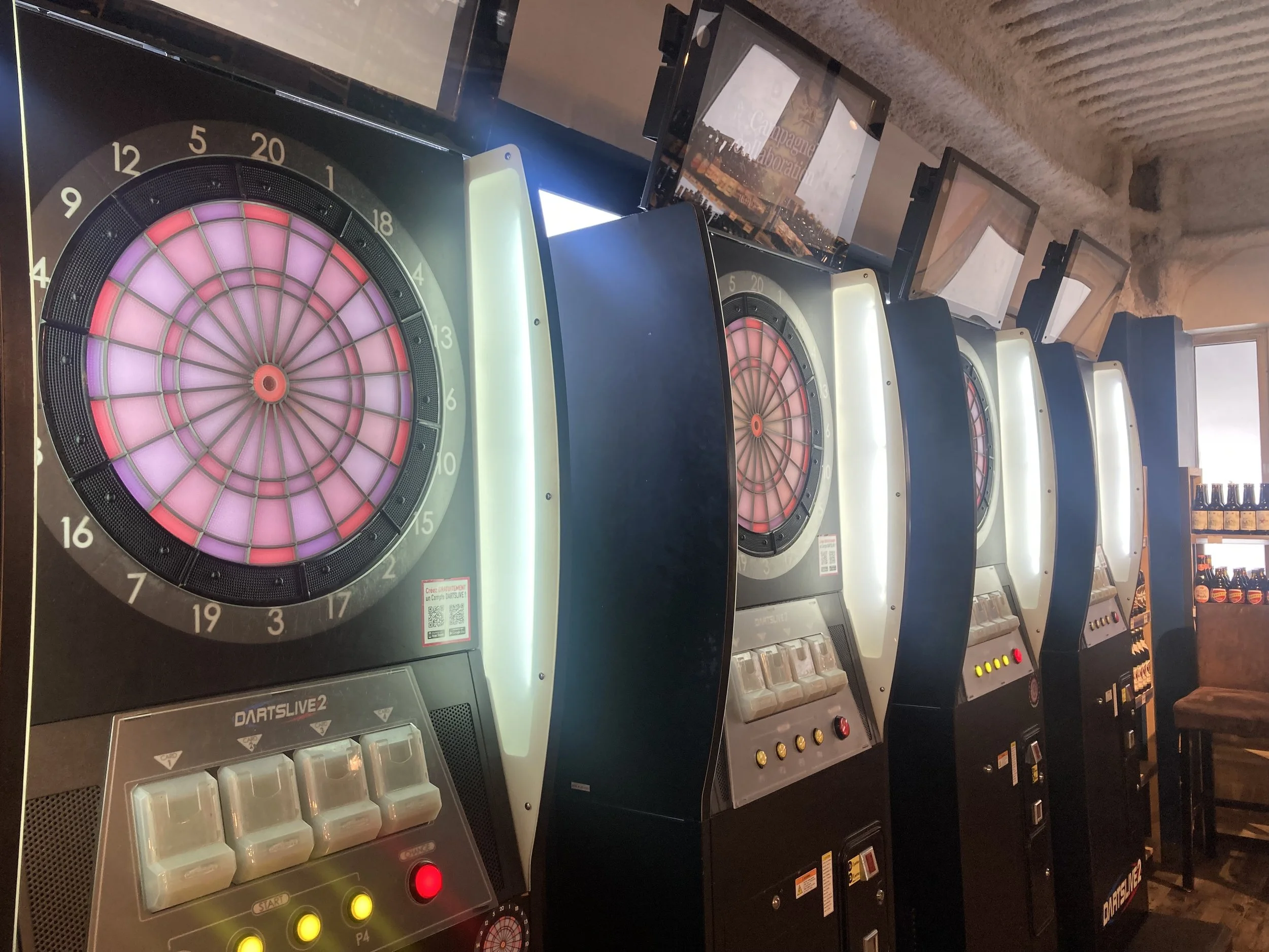 Une rangée de machines de jeu électronique de fléchettes, avec une cible lumineuse et des boutons de commande.