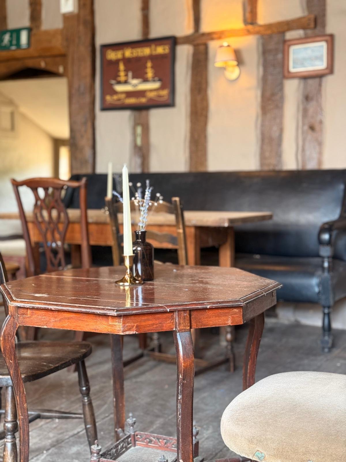 The Swan Inn Hoxne - Interior of a cozy restaurant with wooden furniture, decorated with candles and a small flower arrangement on a table, featuring vintage-style decor and wood-paneled walls.