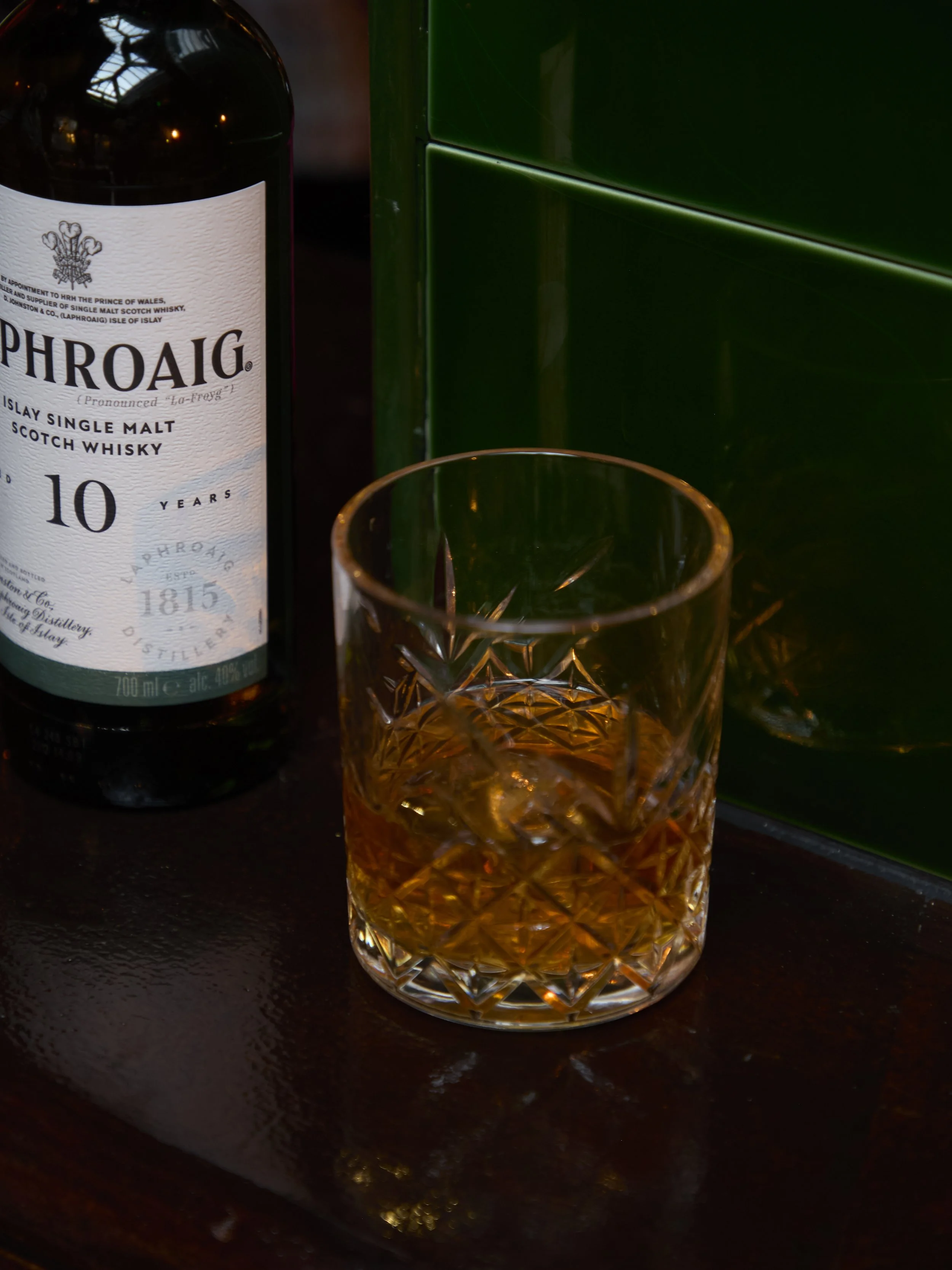 A glass of whiskey with ice on a dark wooden surface next to a bottle of Laphroaig 10-year-old single malt scotch whisky.