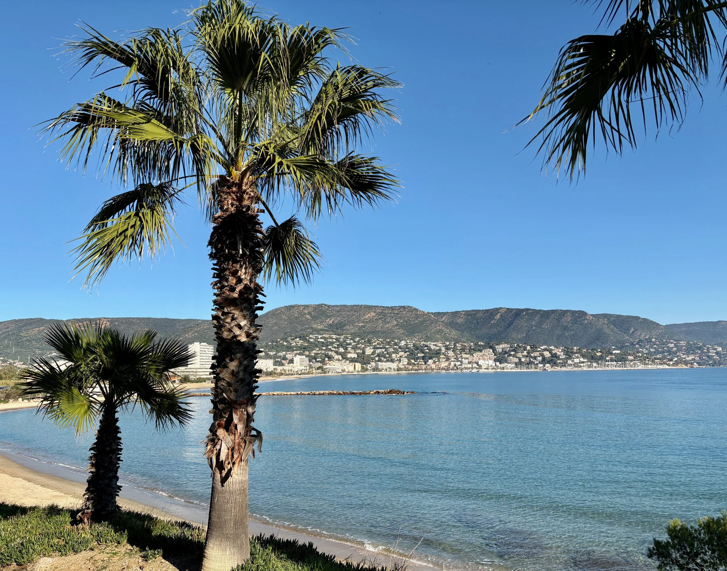 The coastal boardwalk of Le Lavandou along a clear, sunny Mediterranean sea.