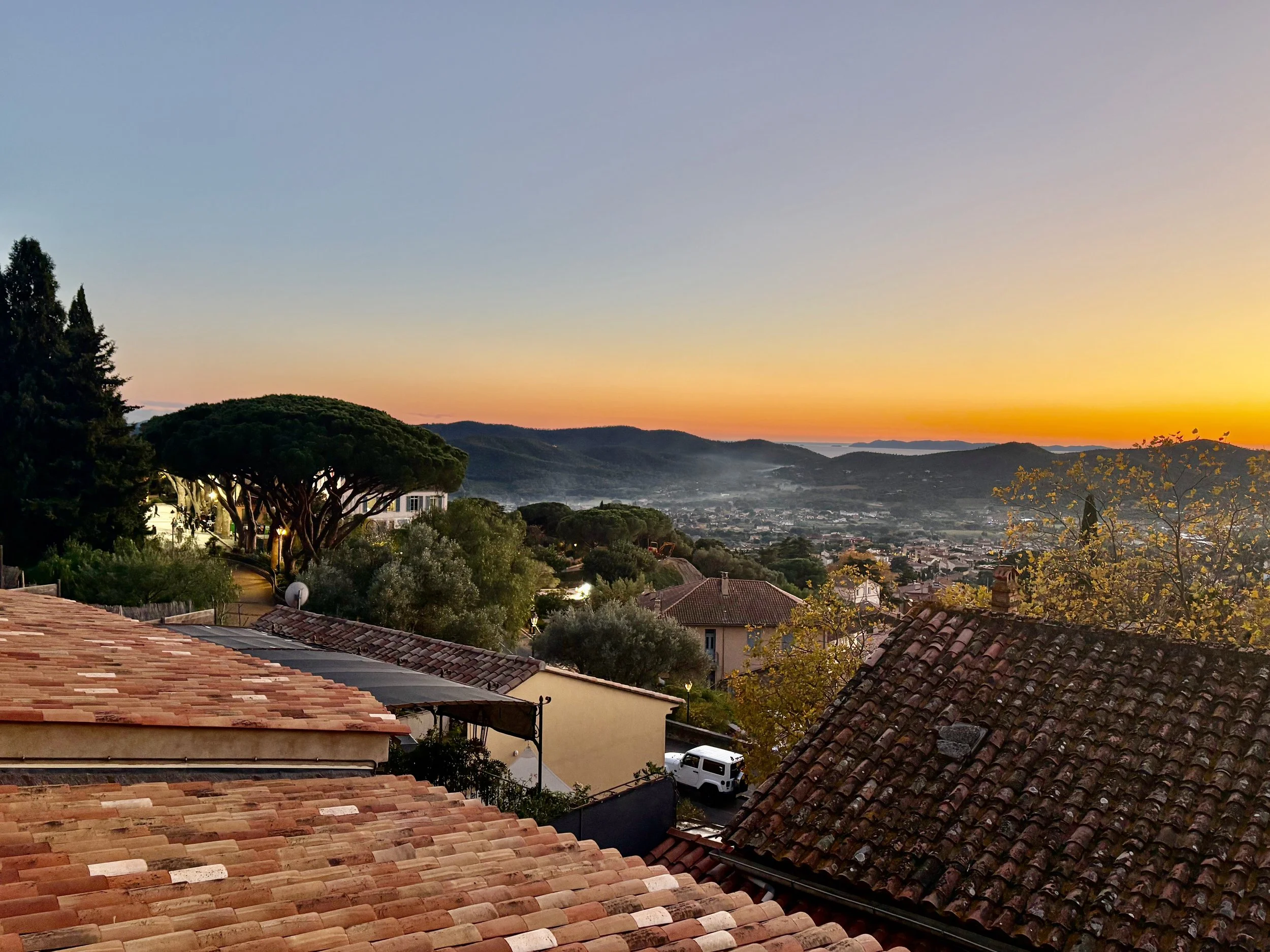 Rooftops of Bormes-les-Mimosas, France with a valley below draped in fog and wood smoke at sunset.