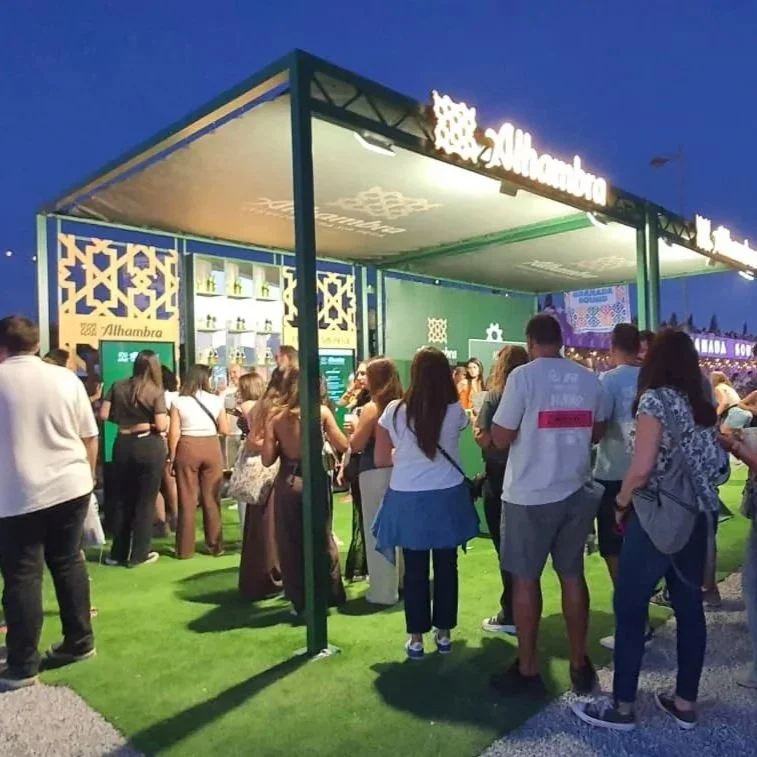 Grupo de personas en un festival con un stand de la empresa "Alhambra" haciendo cola para participar en el juego interactivo desarrollado para la acción de la marca.