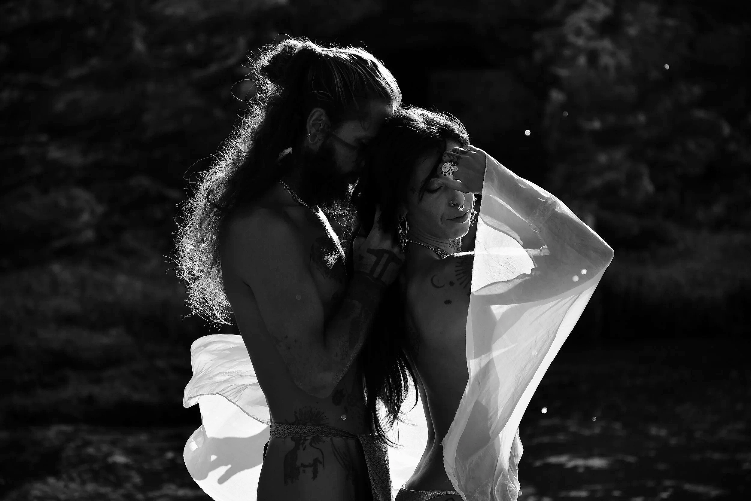 Deux personnes tatouées, dont une porte un voile léger, posant ensemble en plein air avec le soleil brillant en arrière-plan.