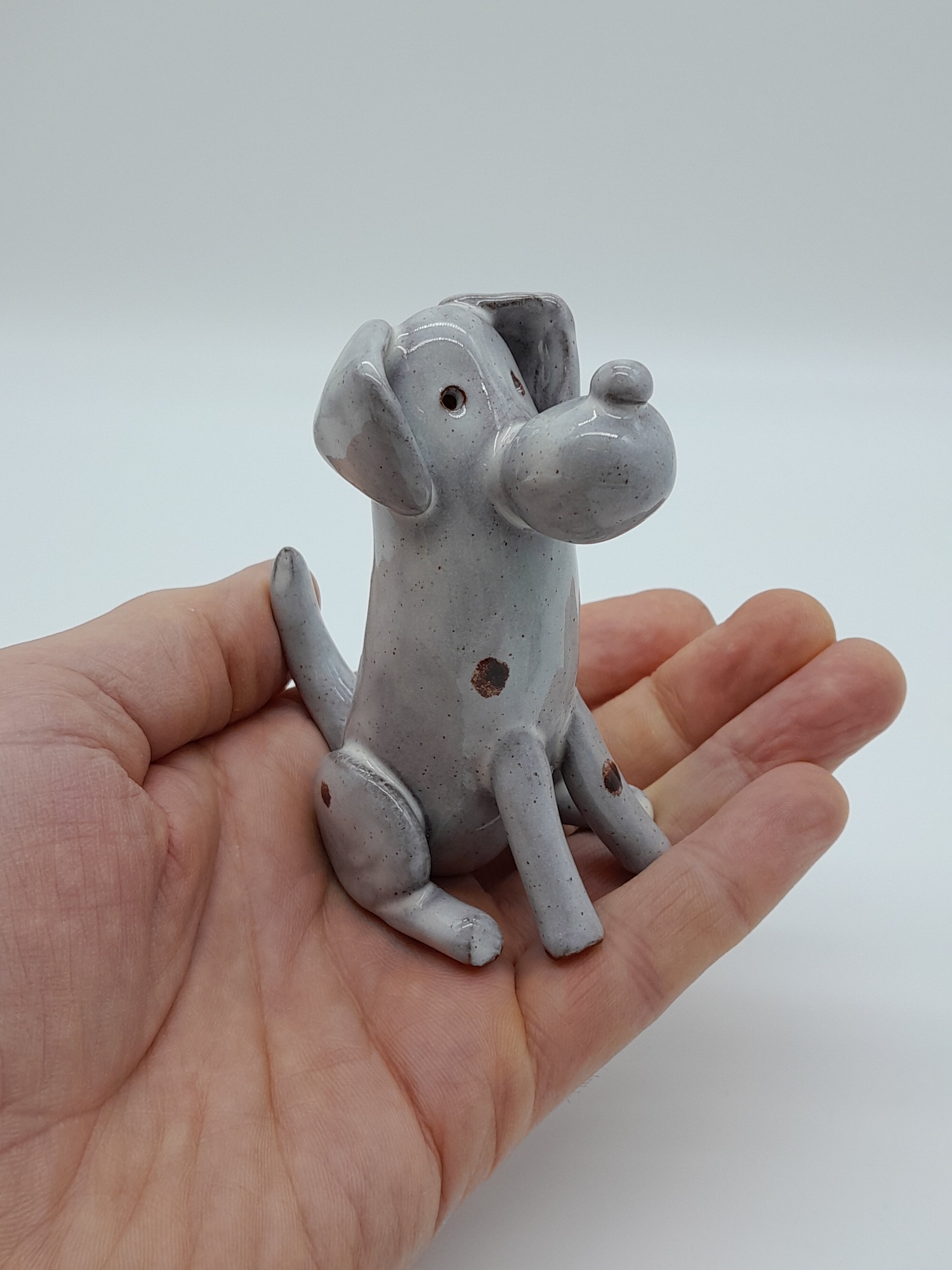 A handmade pottery figurine of a dog in a hand to give a sense of scale
