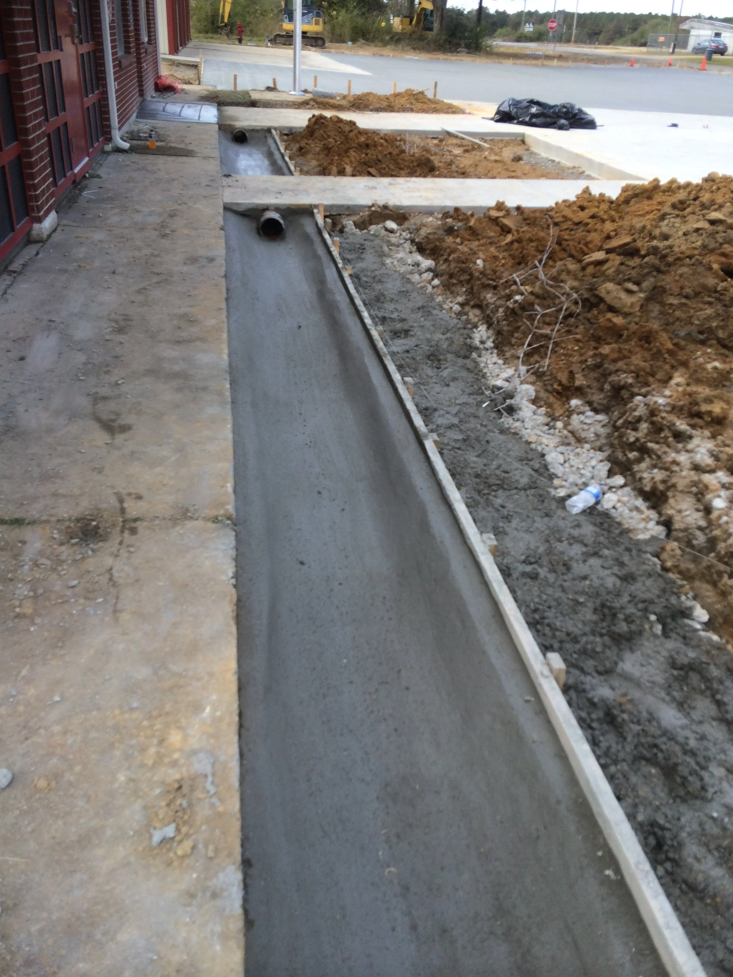Construction site with fresh concrete walkway, dirt, and construction equipment in the background.