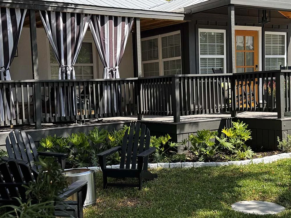 Backyard patio with black wooden deck, outdoor furniture, and a small garden with green plants and bushes.