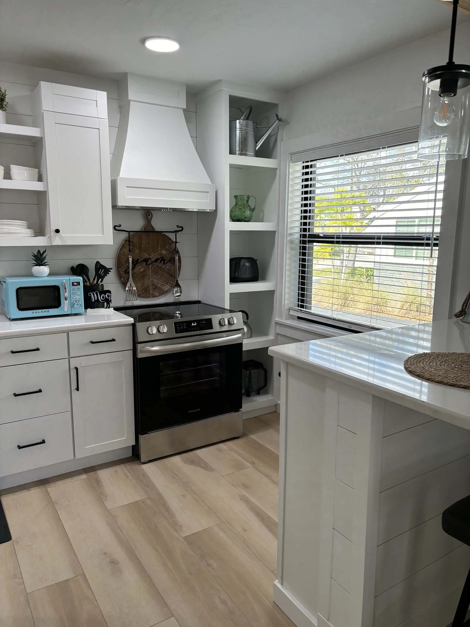 Kitchen with white cabinets, a black stove, a window with blinds, and various kitchen appliances and decor.