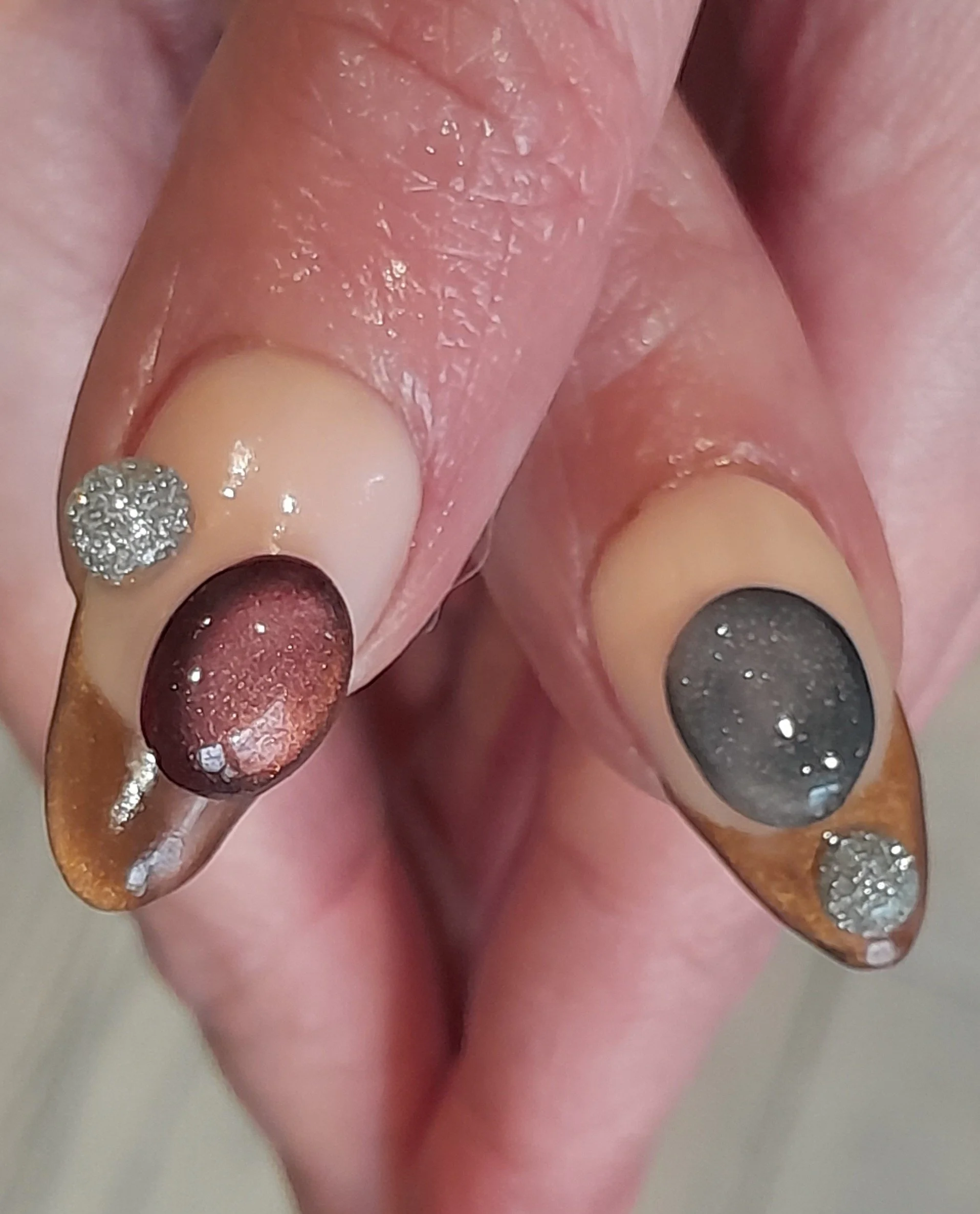 Close-up of a person's hand with decorated nails; both nails have a galaxy design with dark backgrounds and white dots resembling stars, and additional rhinestones on the tips.