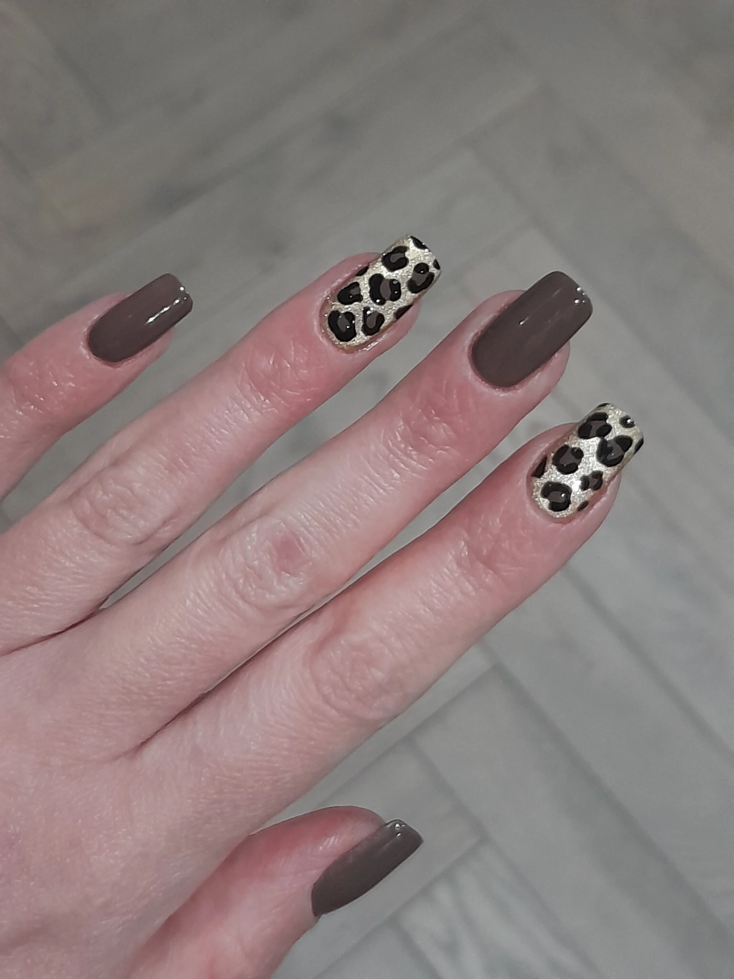 Hand with brown and leopard print nail polish.