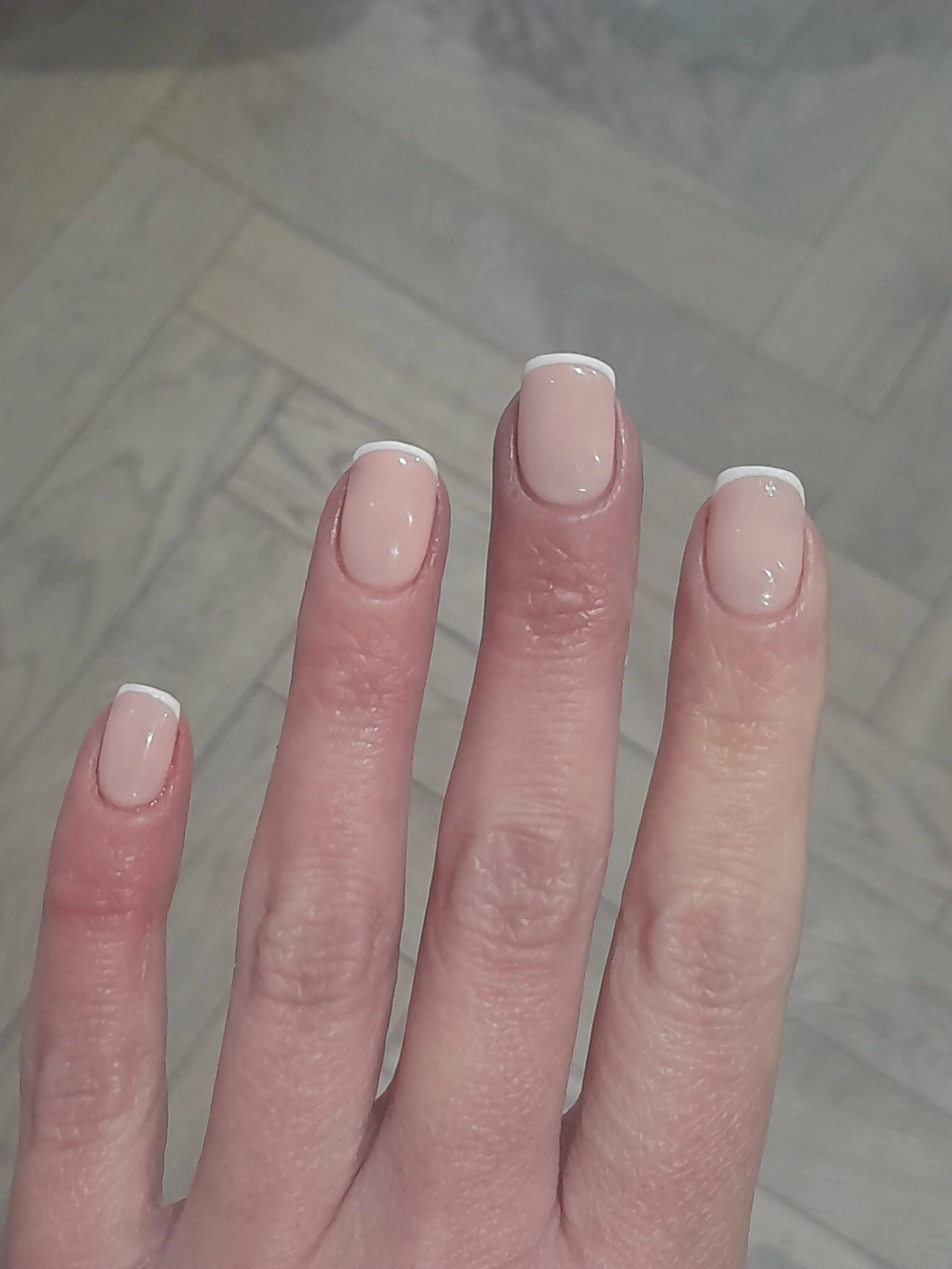Close-up of a hand with neatly manicured nails painted with a French tip style, featuring a natural pink base and white tips.