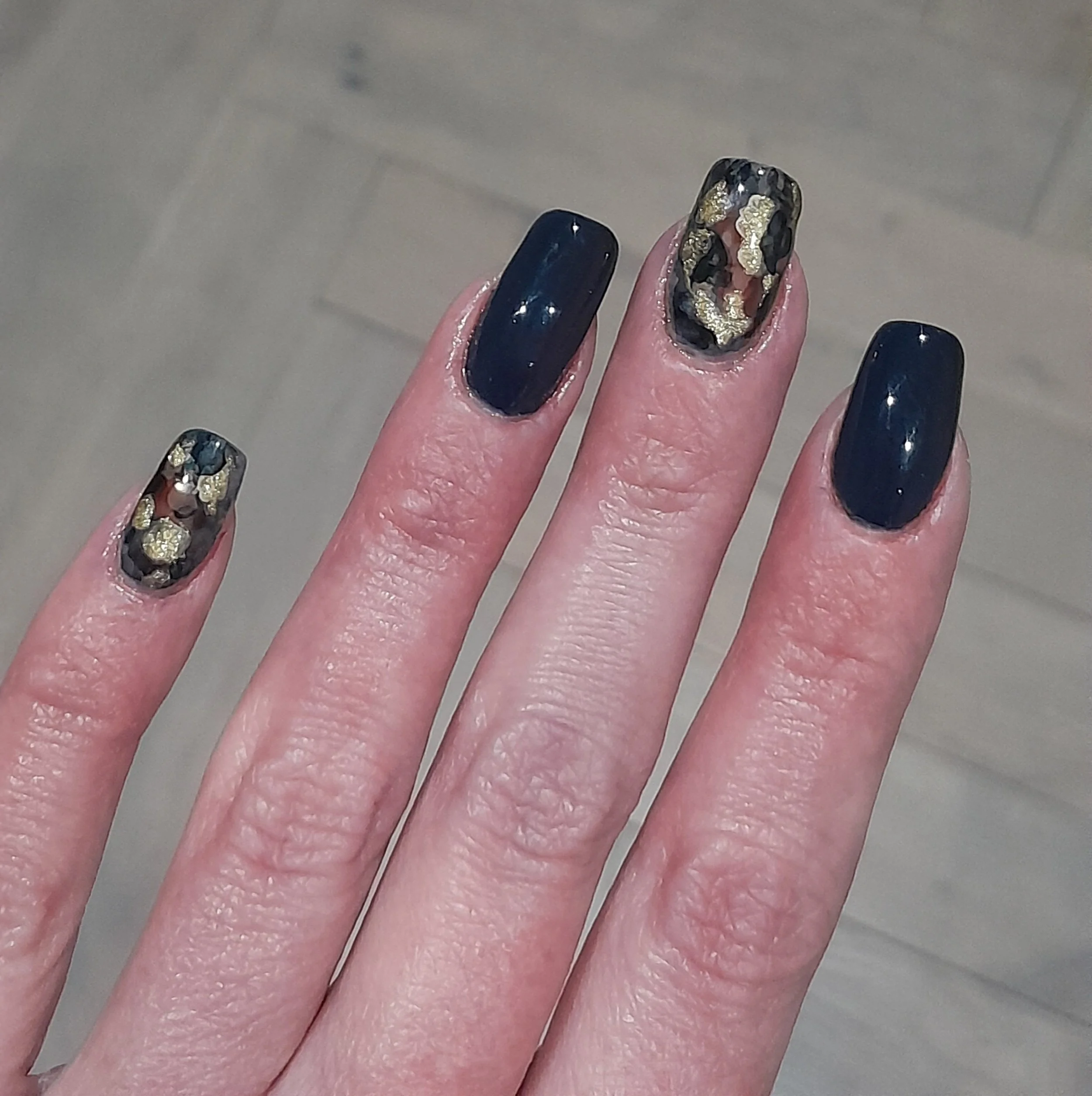 A hand with four fingers showing, featuring dark navy blue and leopard print nail designs with gold accents.