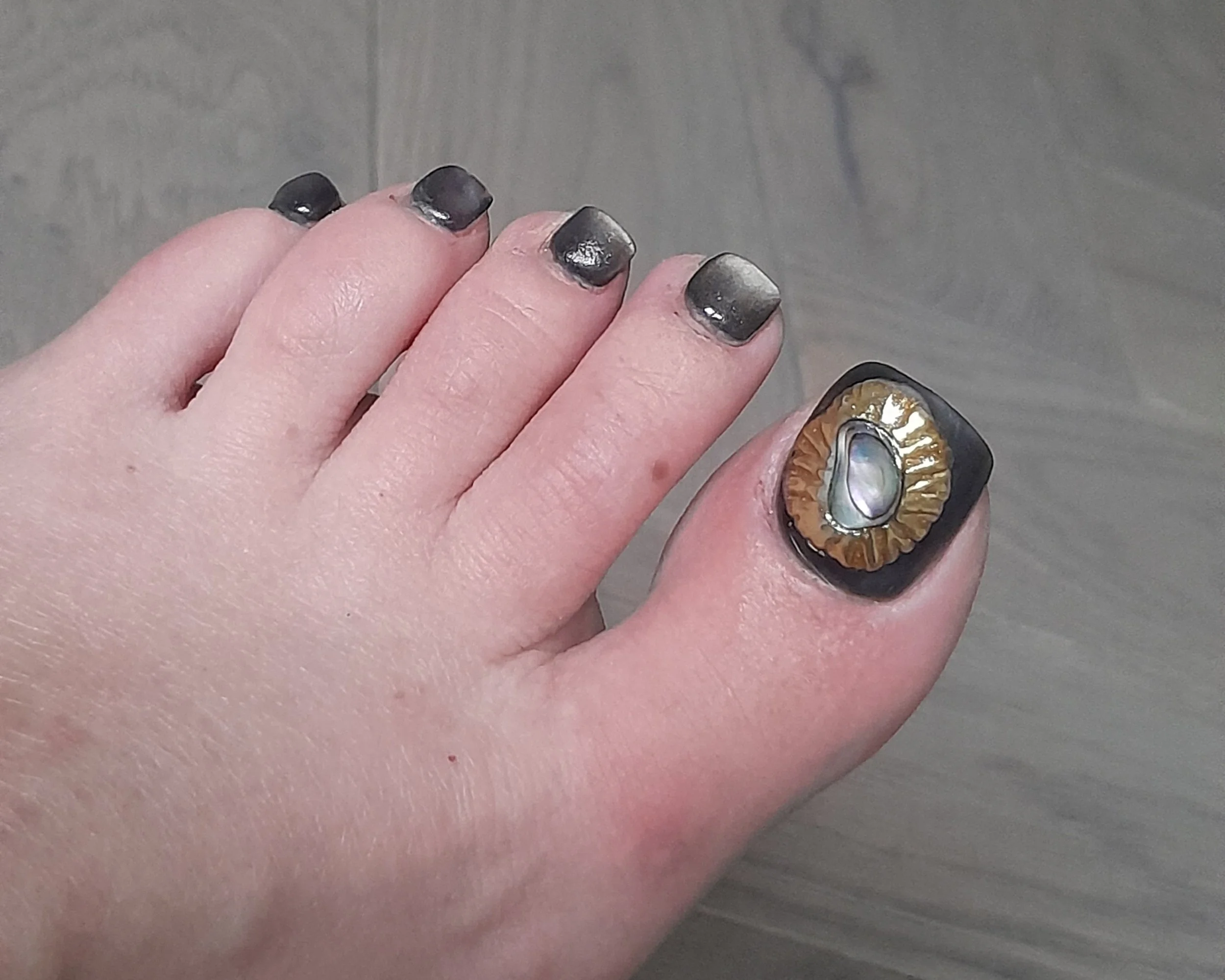 Close-up of a big toe with black nail polish and a decorative ring with a pearl in the center.