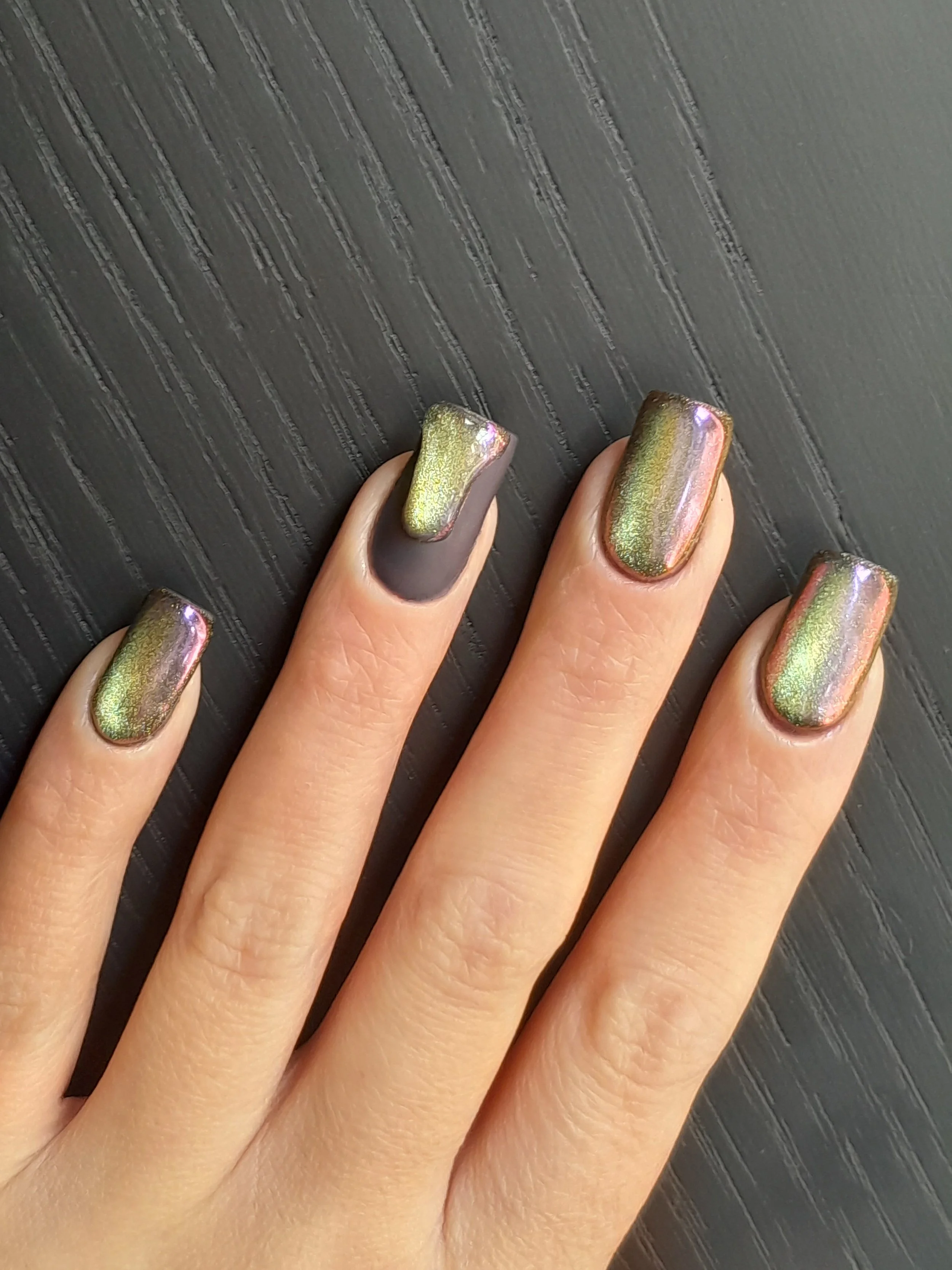 Close-up of a hand with multi-color metallic and matte nail polish on fingers, resting on a textured black surface.