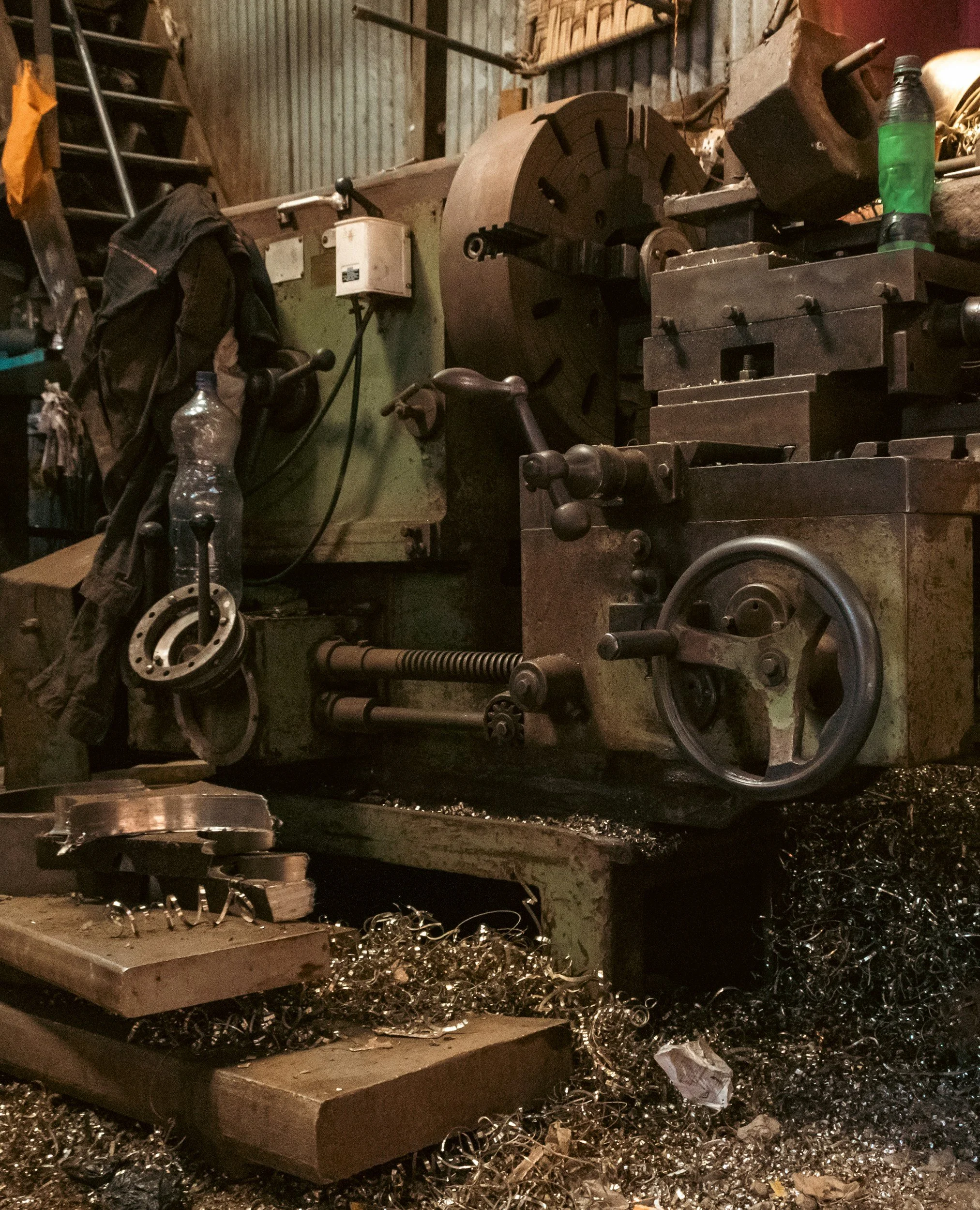 An old industrial lathe machine in a workshop with metal shavings and parts scattered around.
