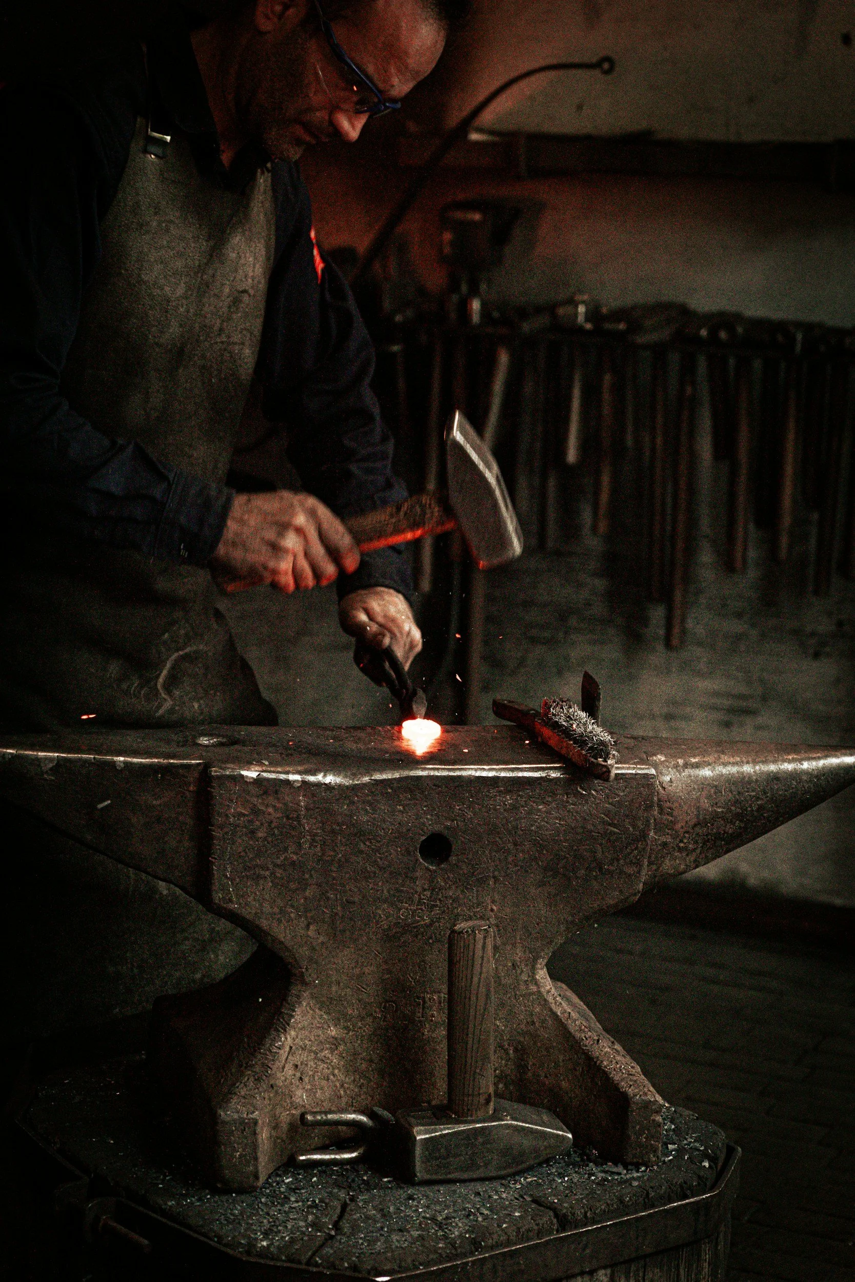 A blacksmith forging metal on an anvil in a workshop, holding a hammer and working on a piece of glowing metal.