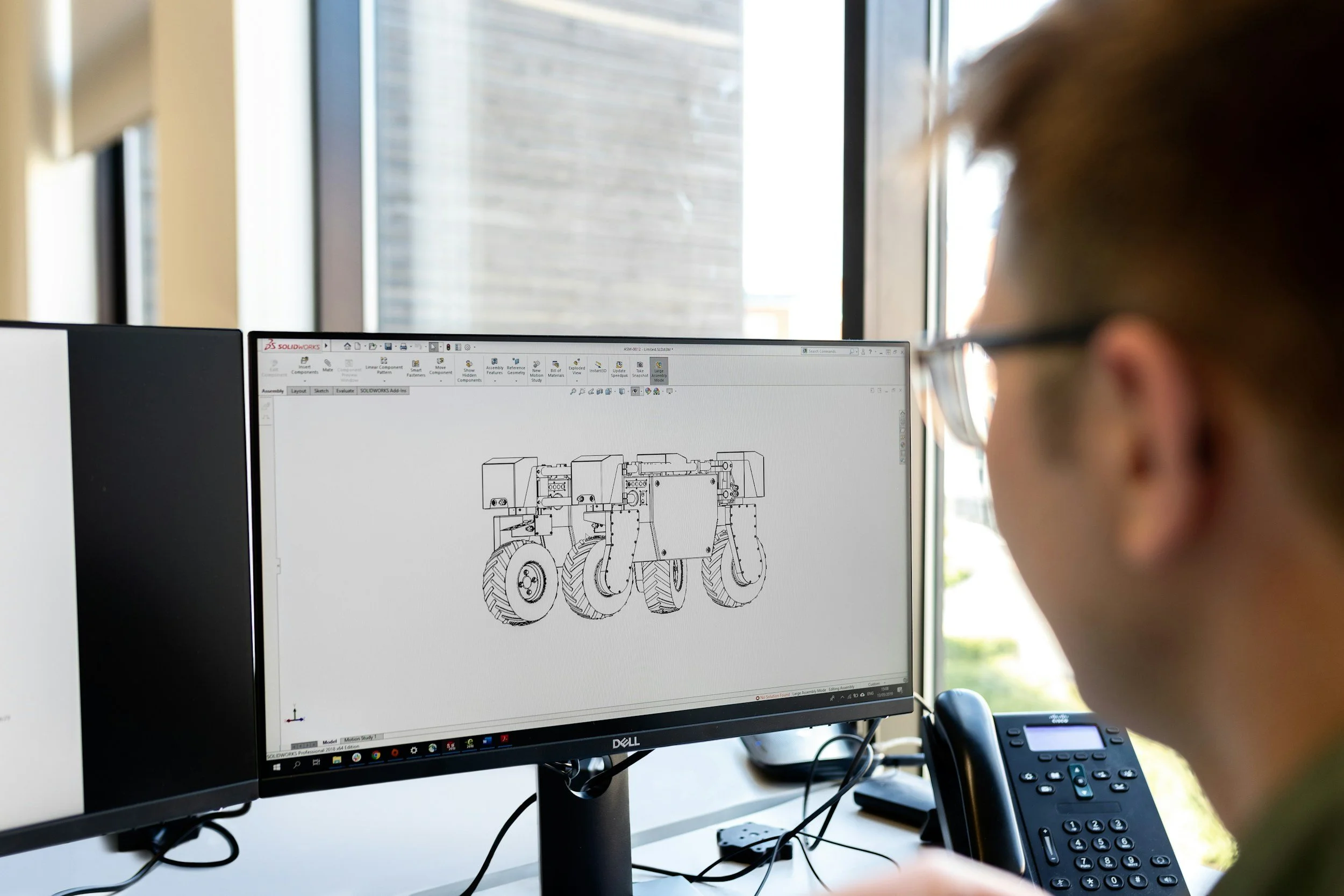 Person working on a computer with a CAD drawing of a machinery design on the screen.