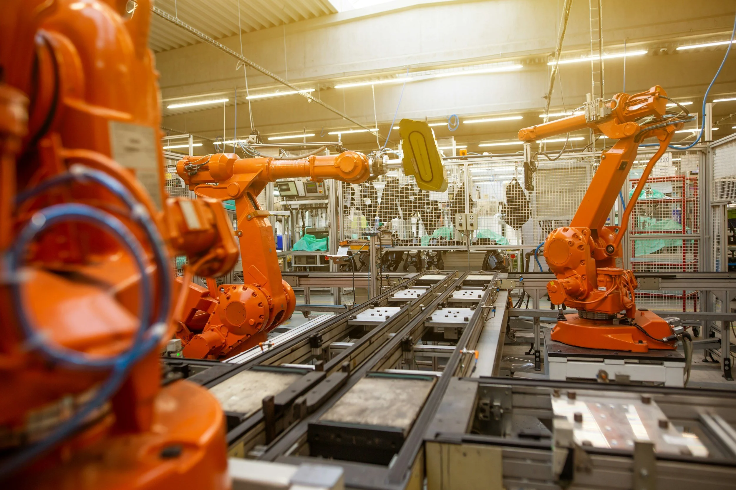 Industrial manufacturing setting with multiple orange robotic arms working on assembly lines, surrounded by machinery and equipment.