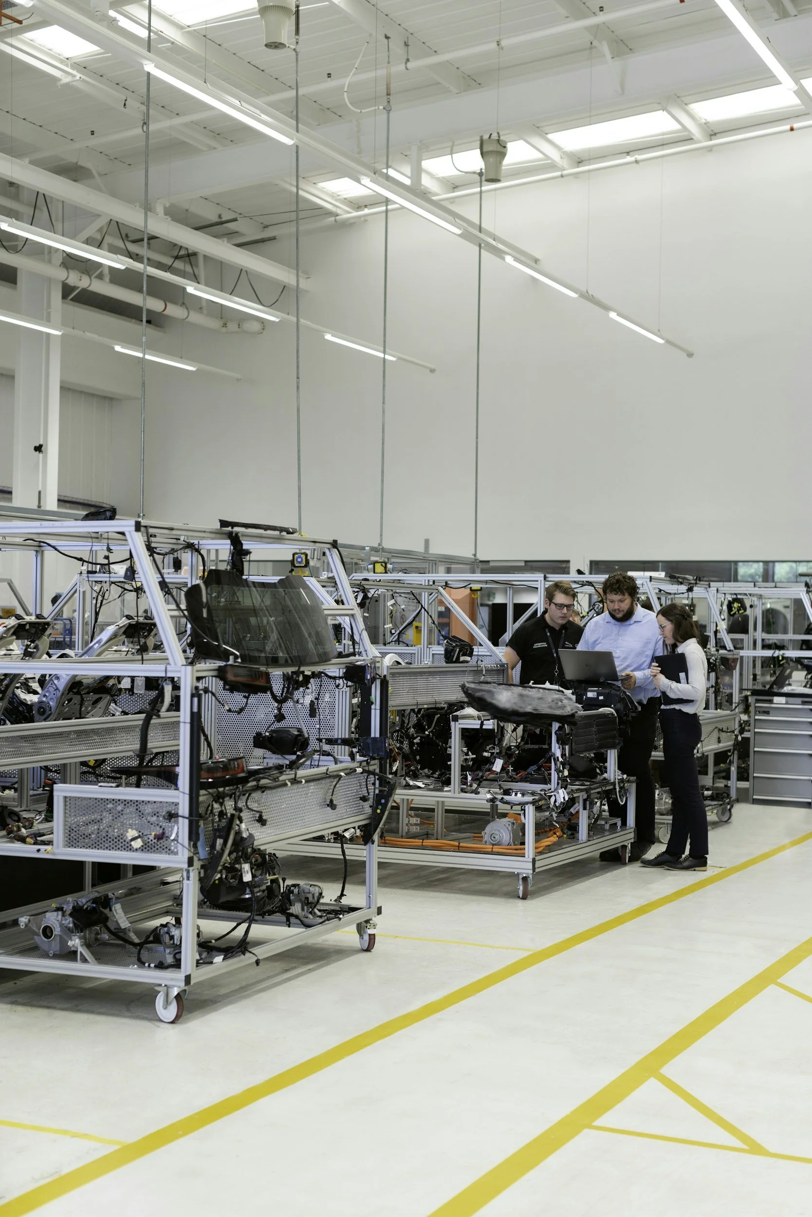 Three engineers inspecting and discussing equipment in a high-tech manufacturing or research facility, surrounded by machinery and workbenches.