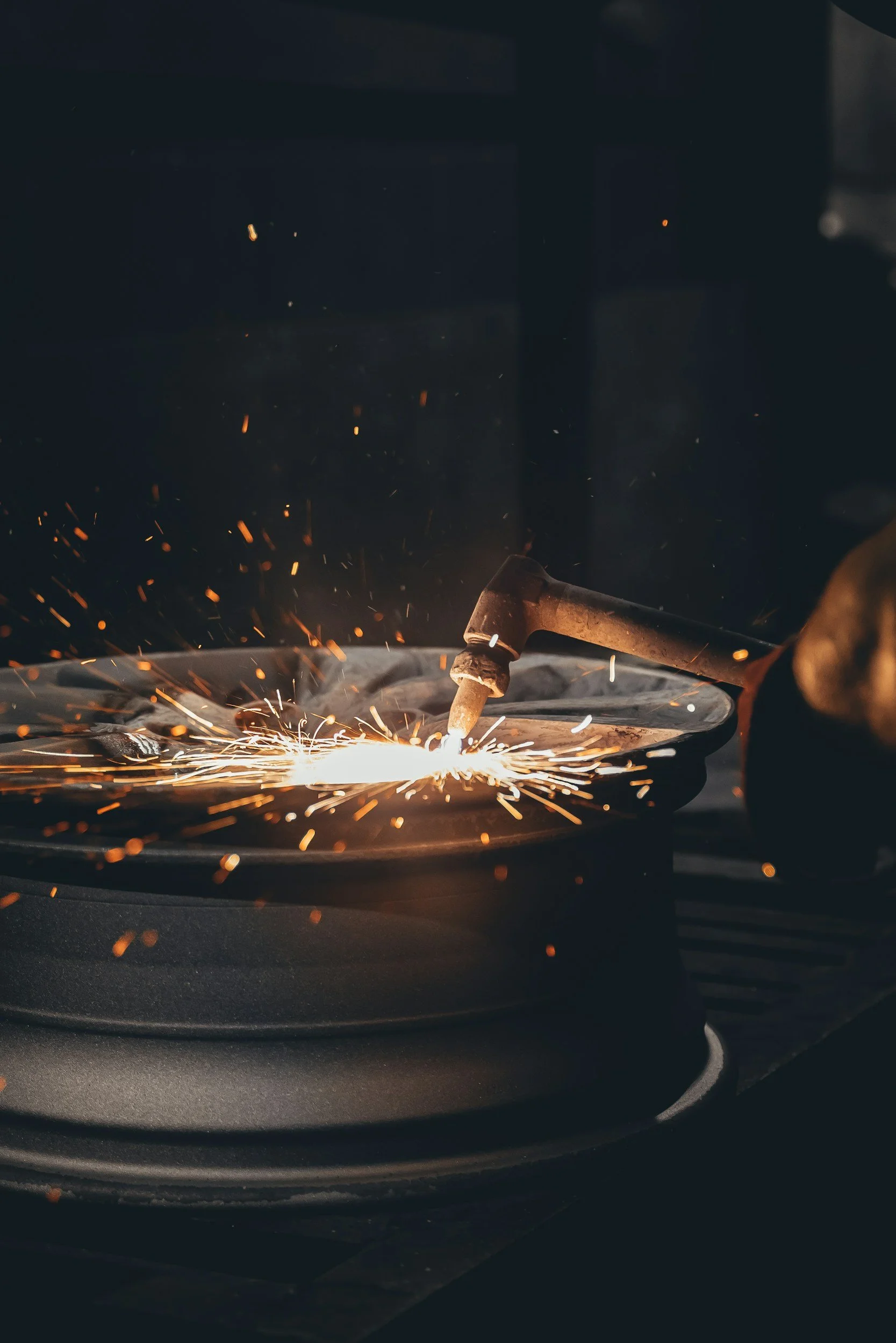 A worker welding metal, sparks flying in a dark industrial setting.