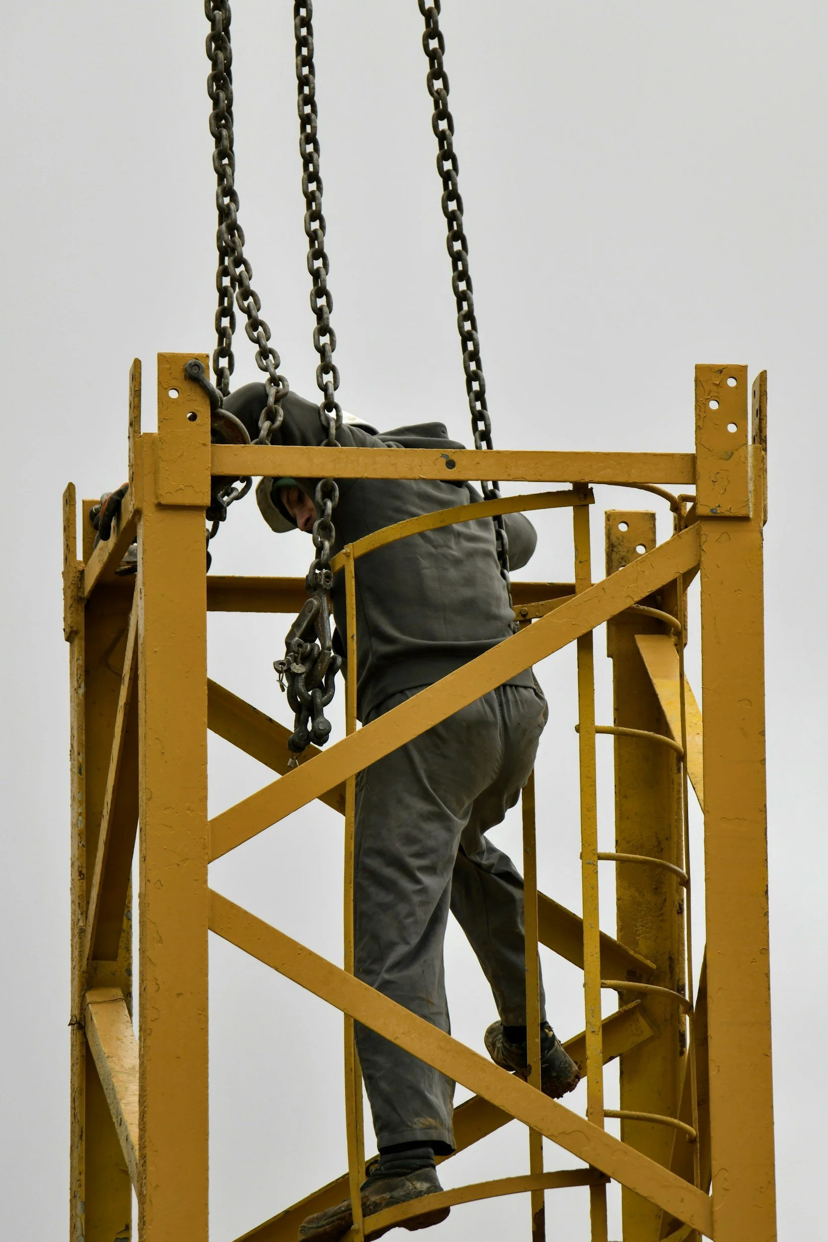 Worker climbing a yellow scaffolding structure against an overcast sky.