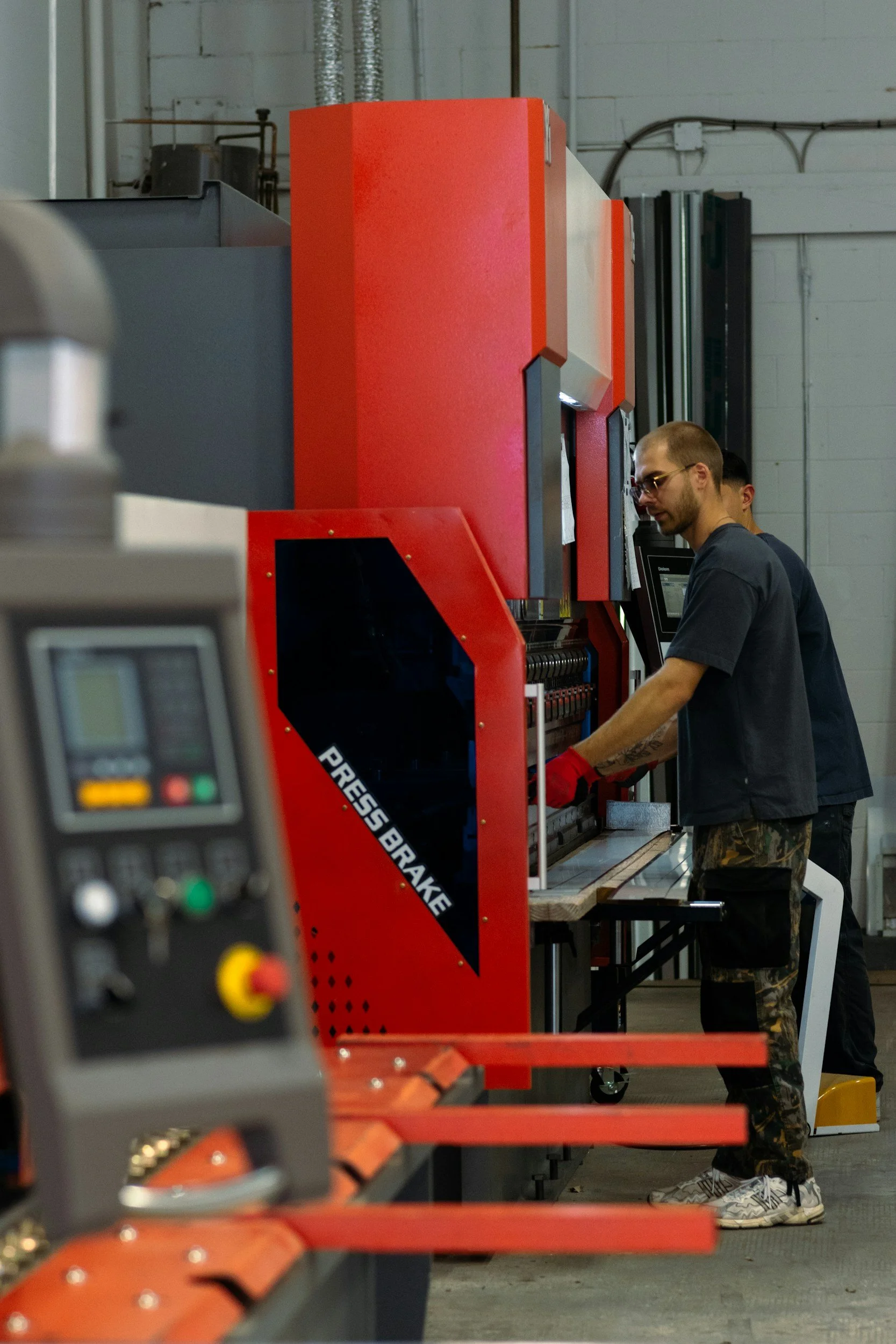 Two workers operating a large red press brake machine in an industrial workshop.