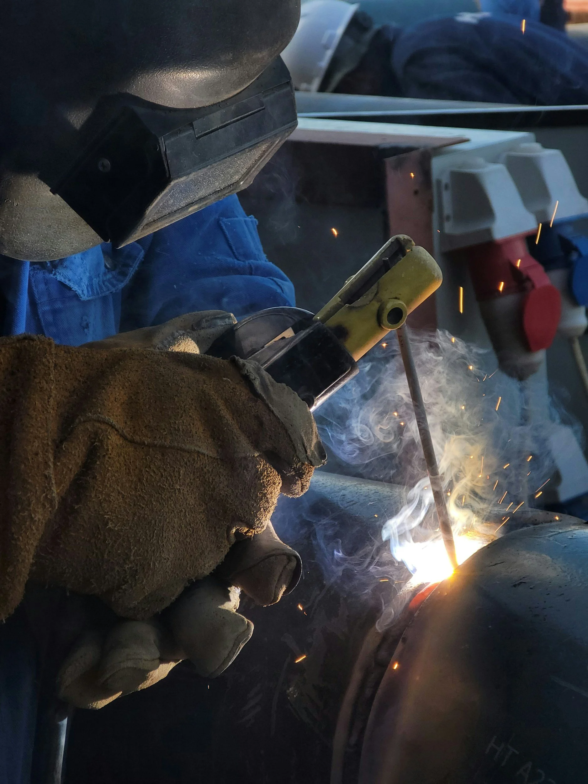 Someone welding metal with a welding torch, sparks and smoke visible, wearing protective gloves and a welding helmet.