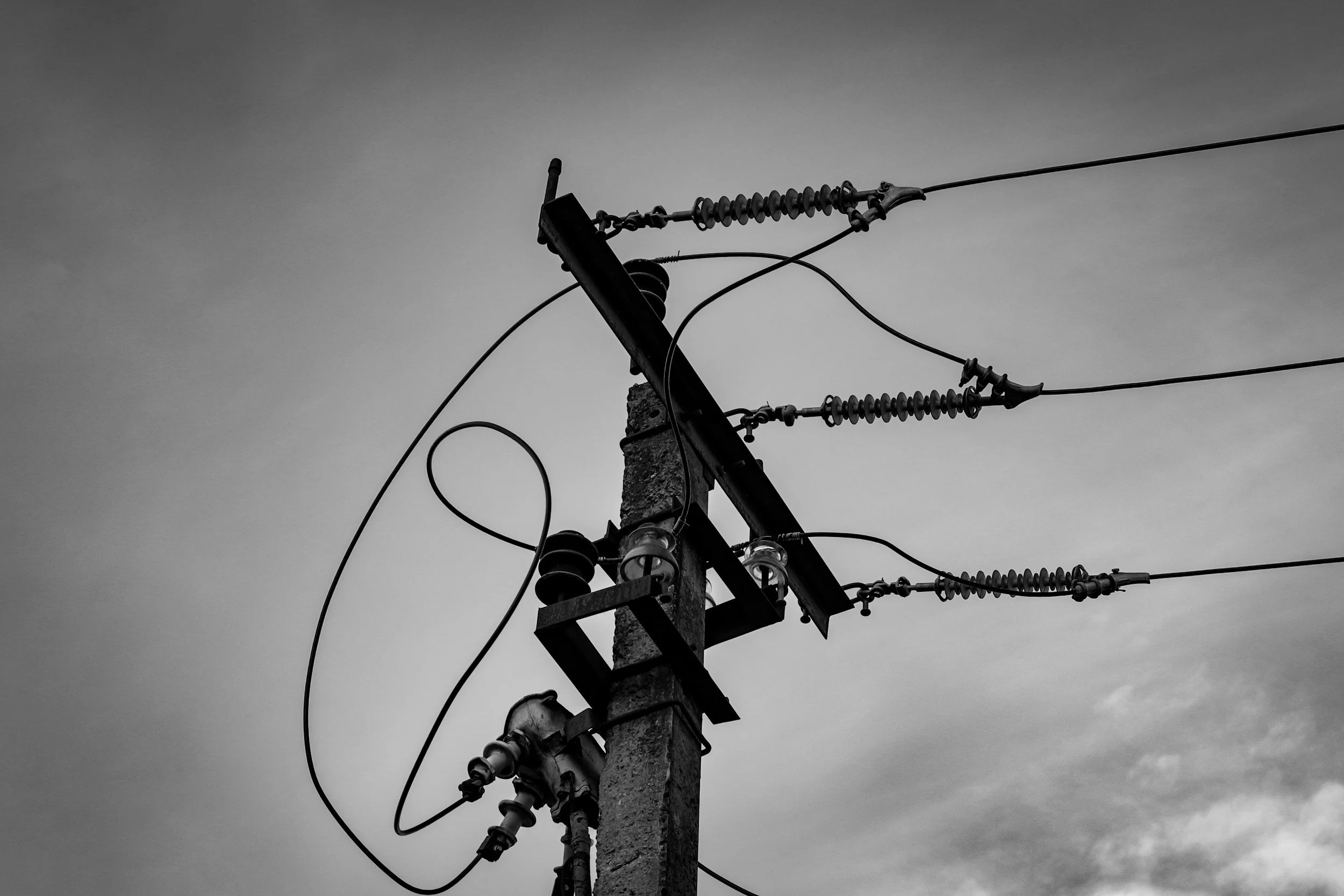 Black and white photo of a utility pole with power lines and insulators against a cloudy sky.
