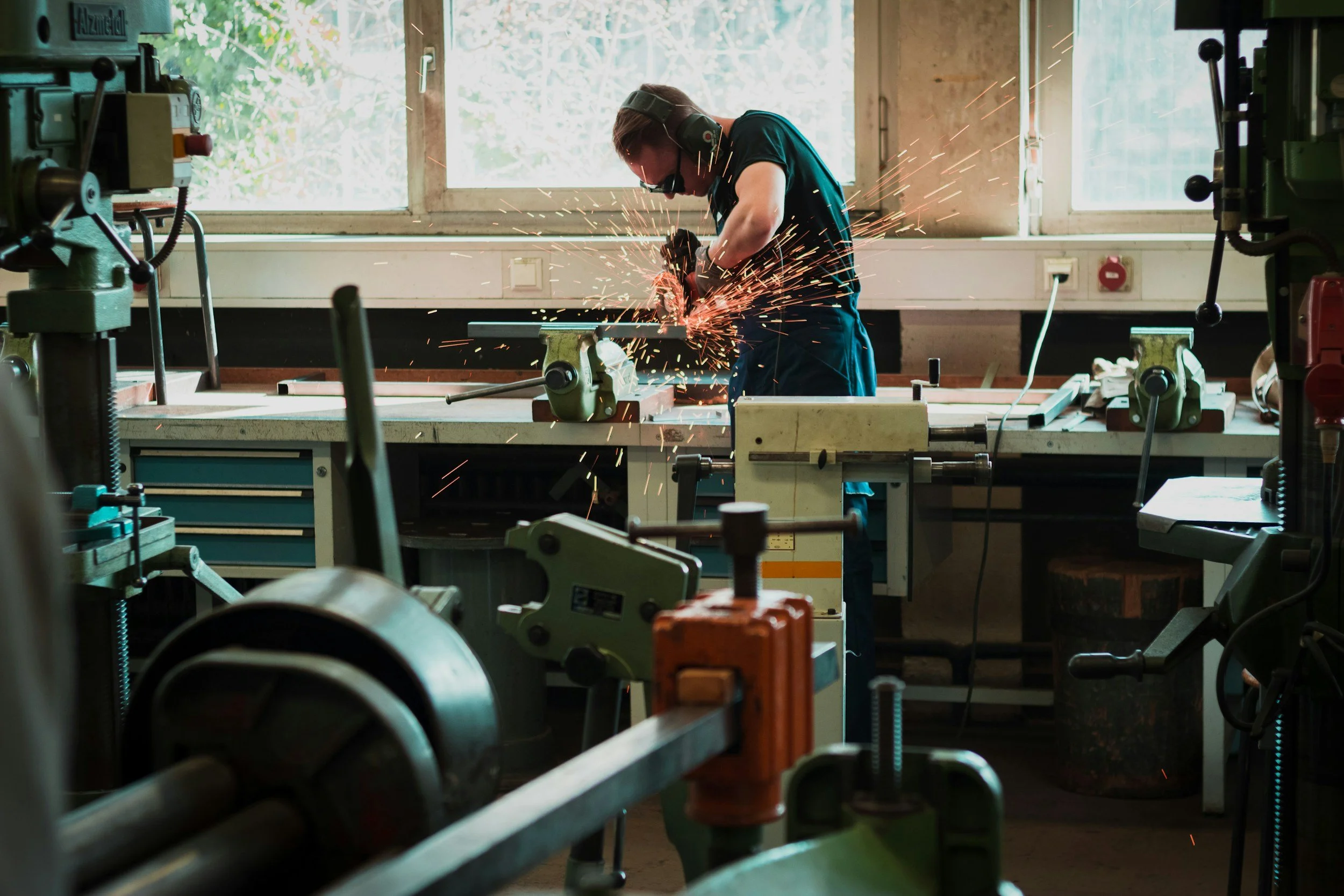 A man welding metal in a workshop with sparks flying, surrounded by various tools and machinery.